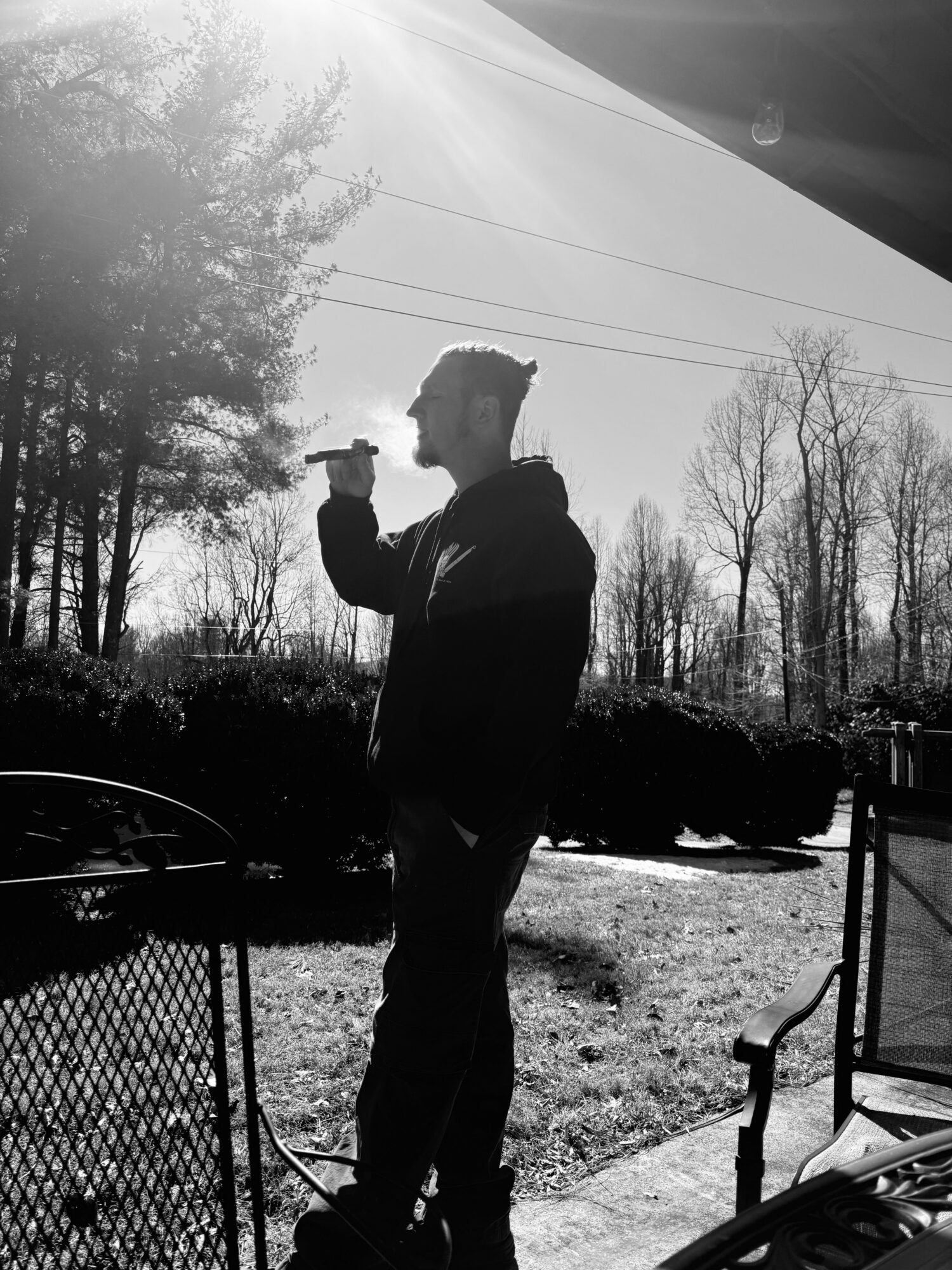 Silhouette of a person standing outdoors, holding an object near their face, with trees and sky in the background.