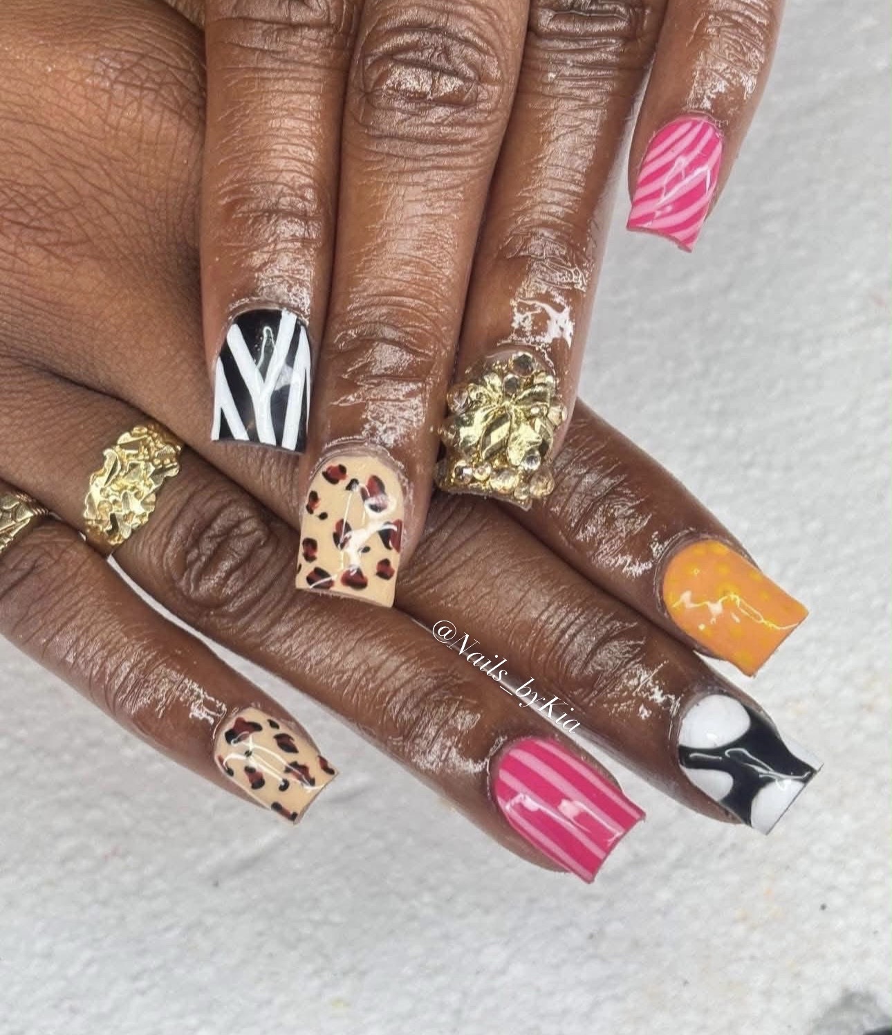 Hands with colorful, patterned nail art and gold rings, showing various animal and abstract designs.