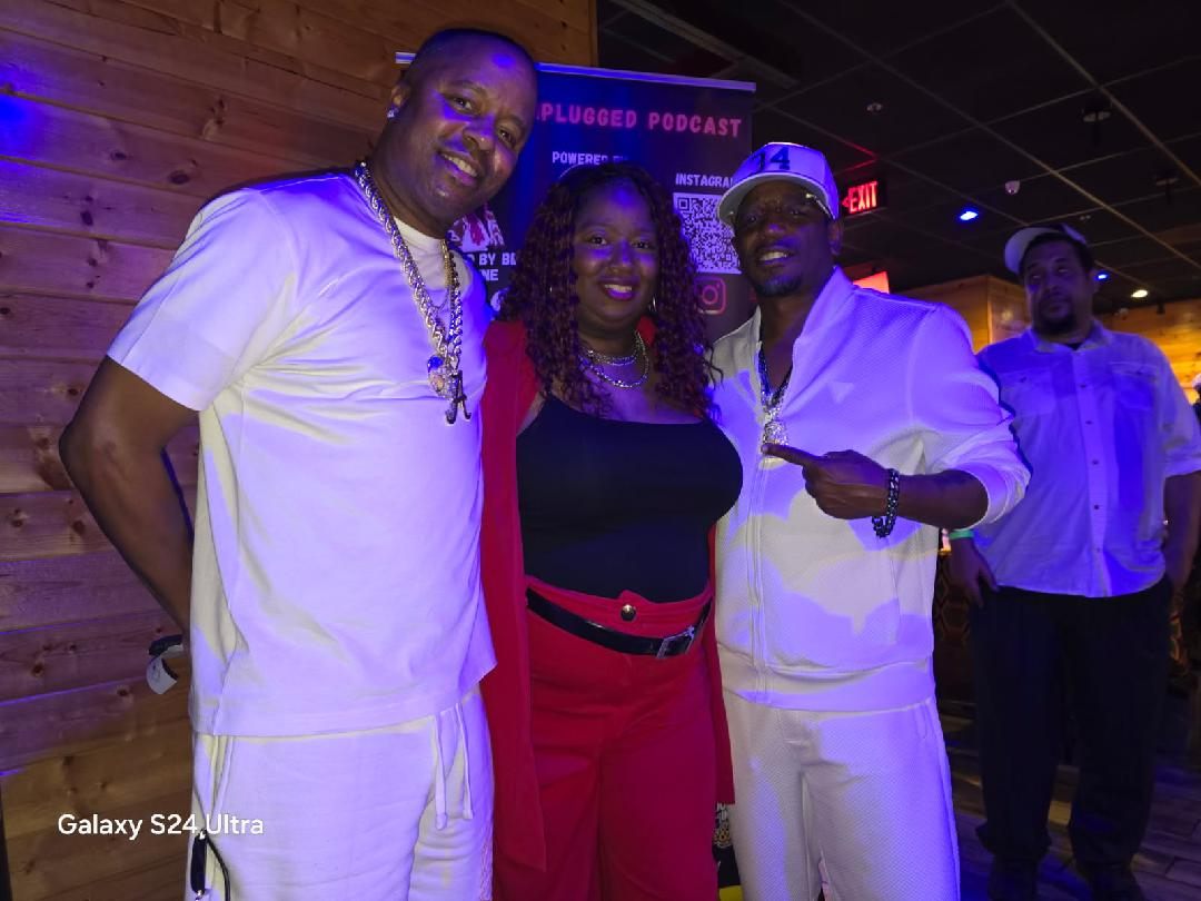 Four people standing together indoors, smiling, with a wooden wall and a screen in the background.