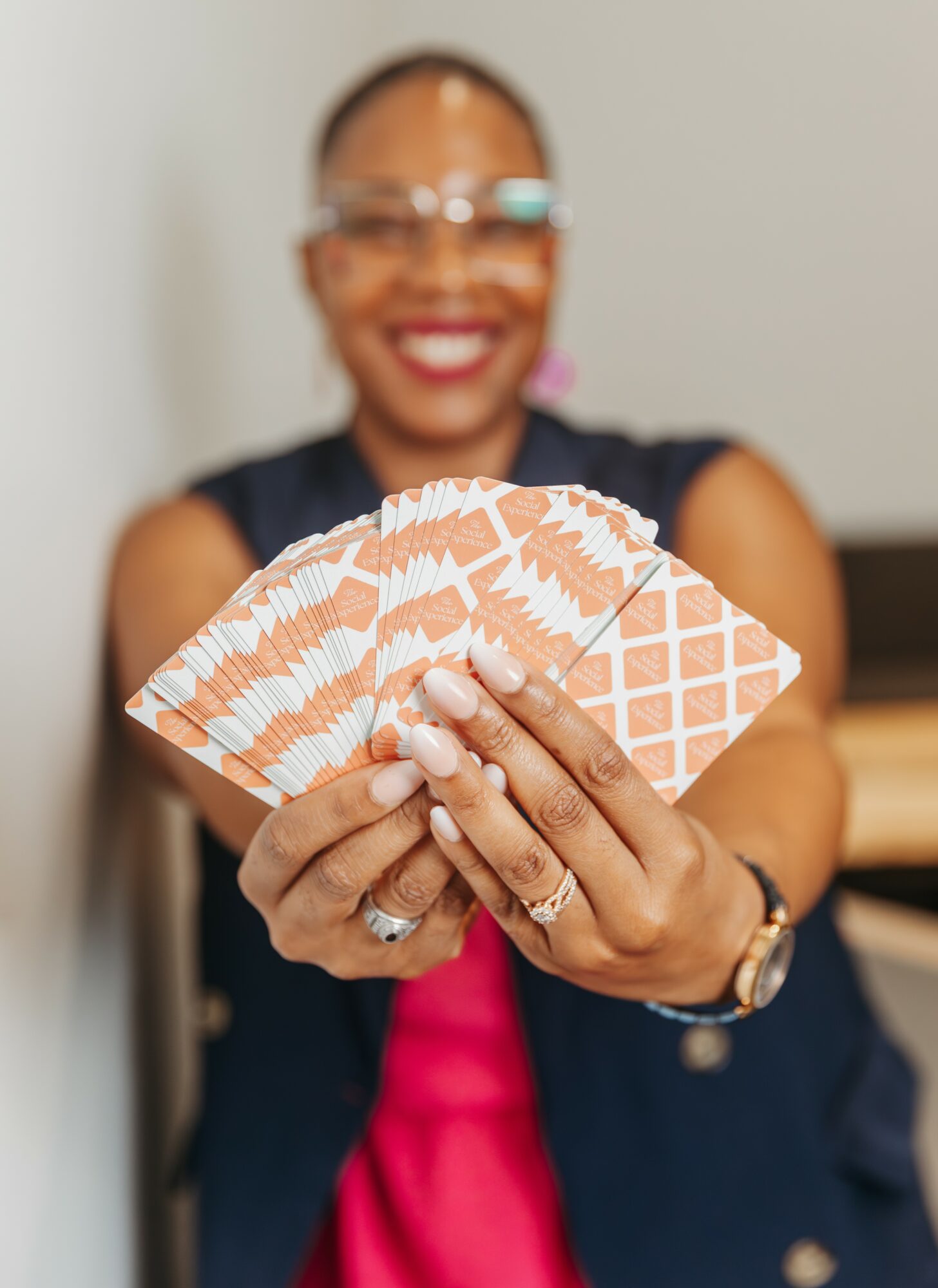 Person holding playing cards, smiling, wearing glasses, with a blurred background.