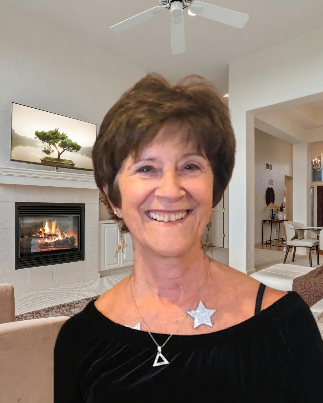 Smiling woman with short brown hair in a living room, wearing a black top and star-shaped necklace.