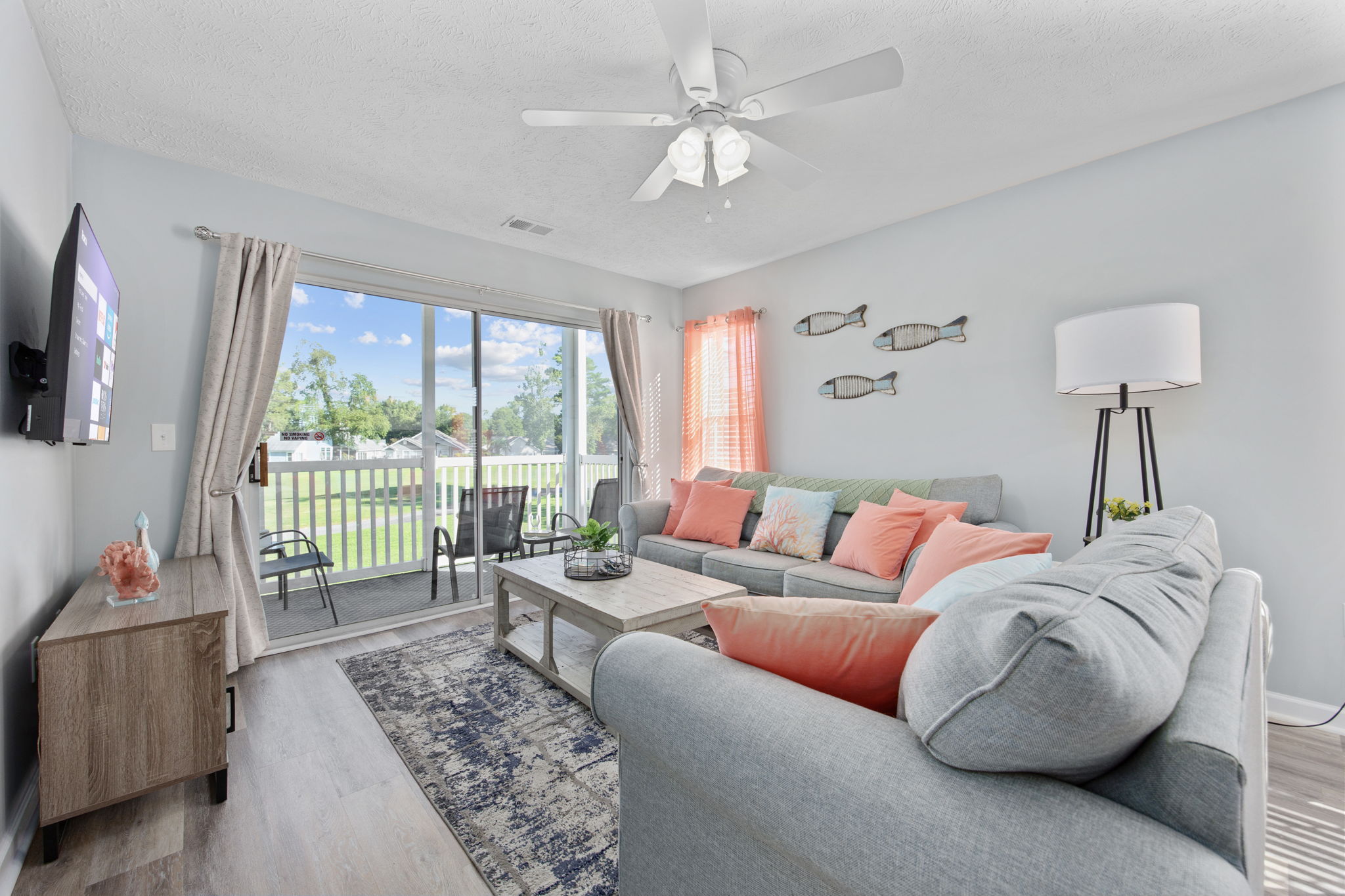 Living room with sofa, coffee table, TV, and sliding glass door leading to outdoor patio, bright and airy space.