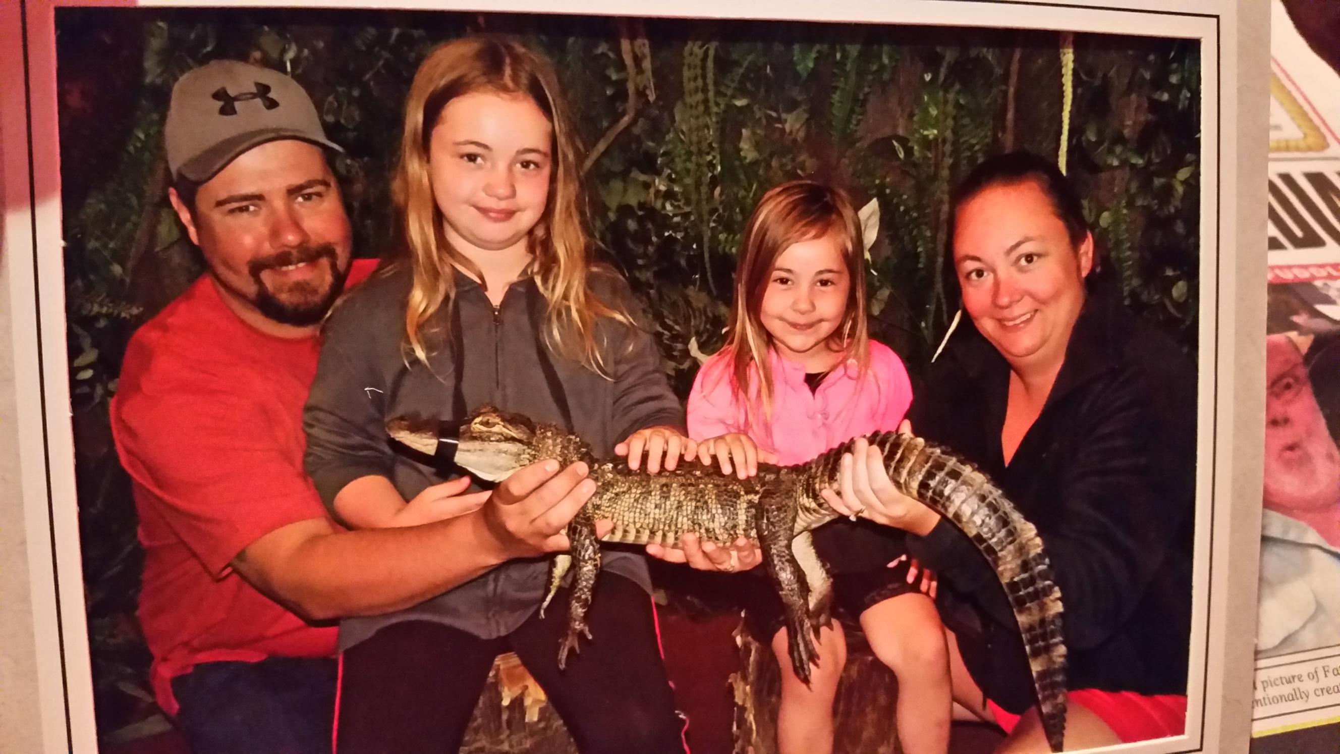 Four people, two children and two adults, holding a small crocodile outdoors, smiling at the camera.