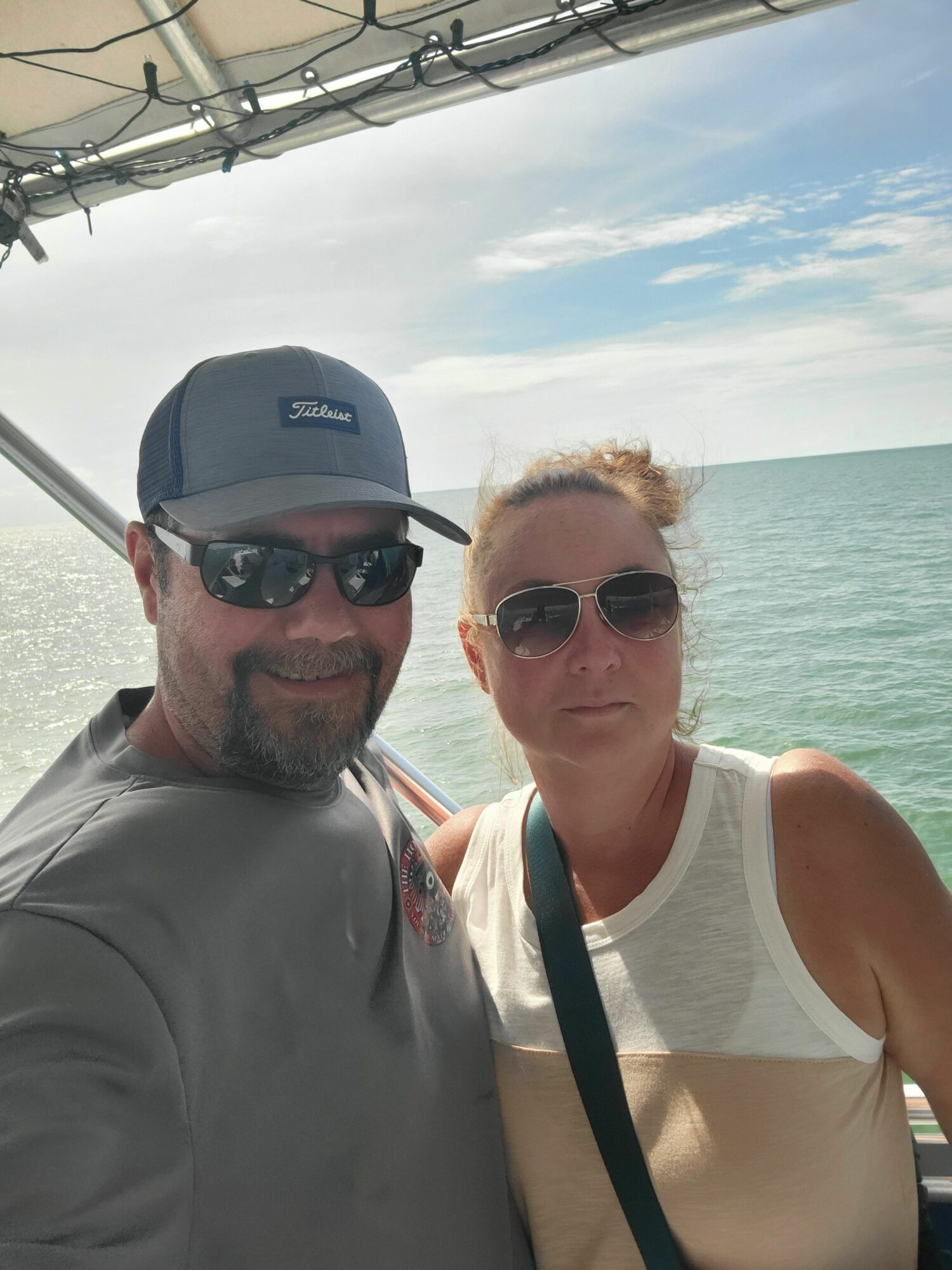 Two people wearing sunglasses and hats on a boat, with water and sky in the background.
