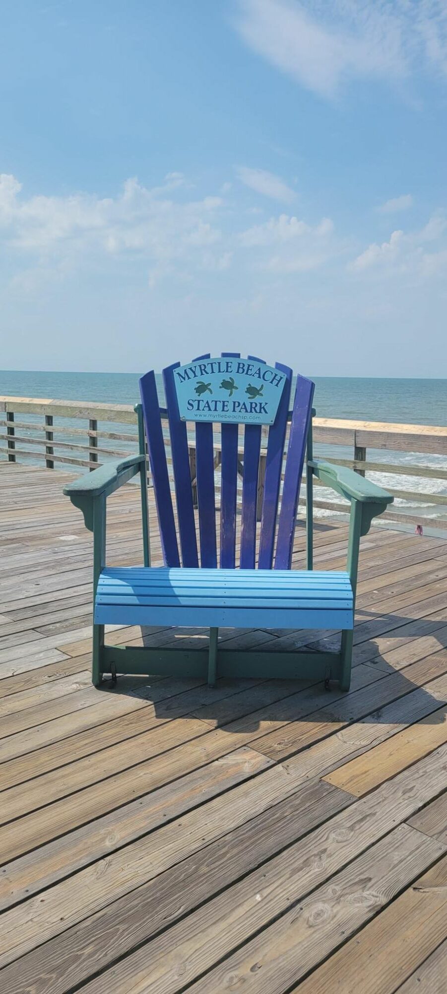 Blue Adirondack chair on a wooden deck with ocean and sky in background.