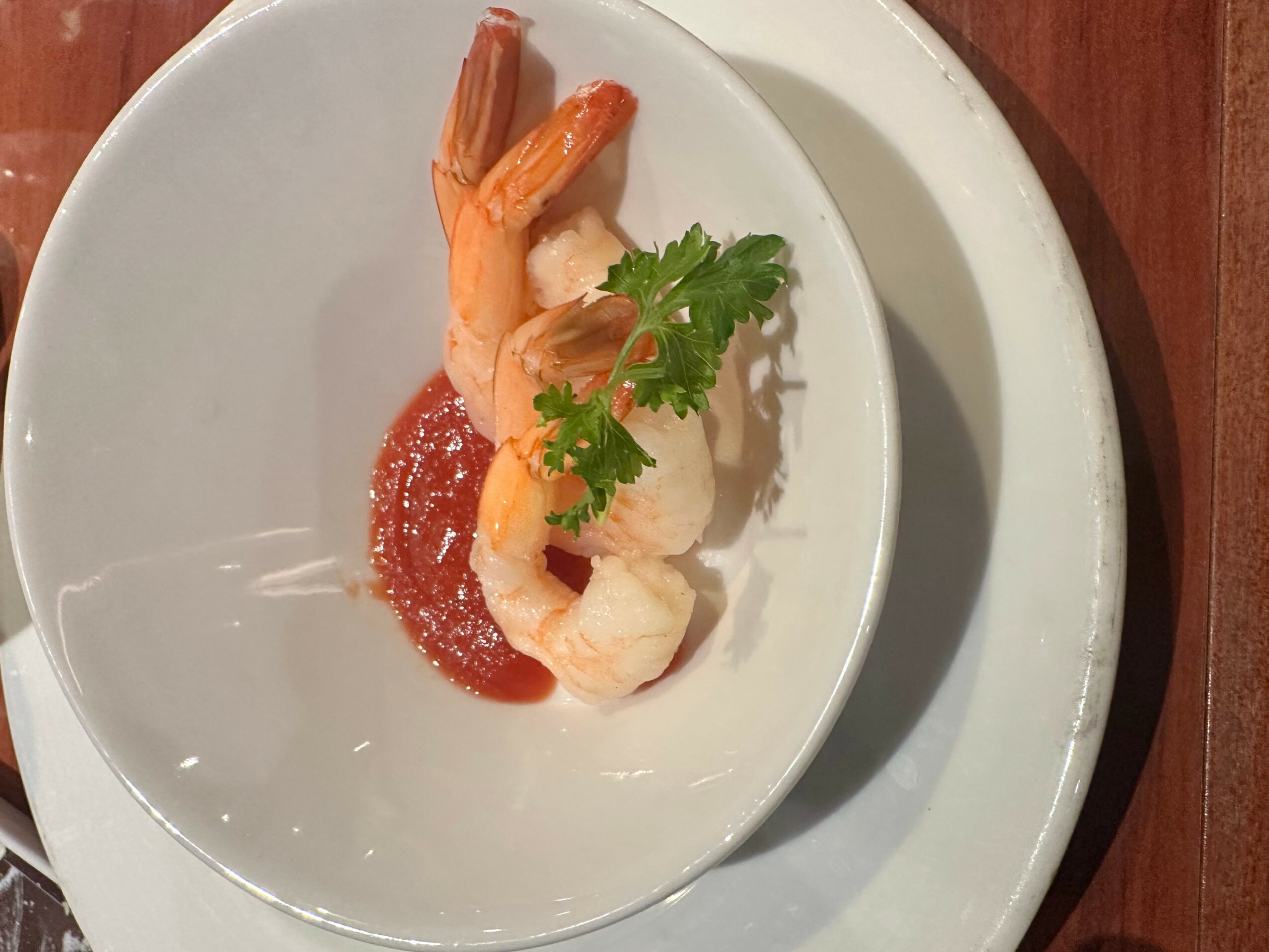Shrimp with sauce and a sprig of cilantro on a white plate, viewed from the side.