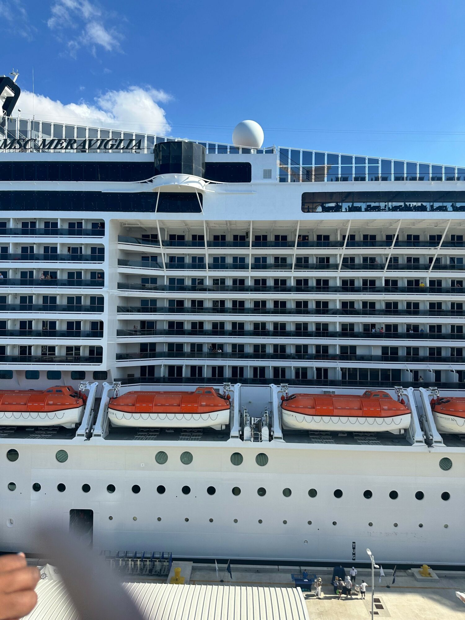 Cruise ship exterior with multiple decks, lifeboats, and a clear blue sky.