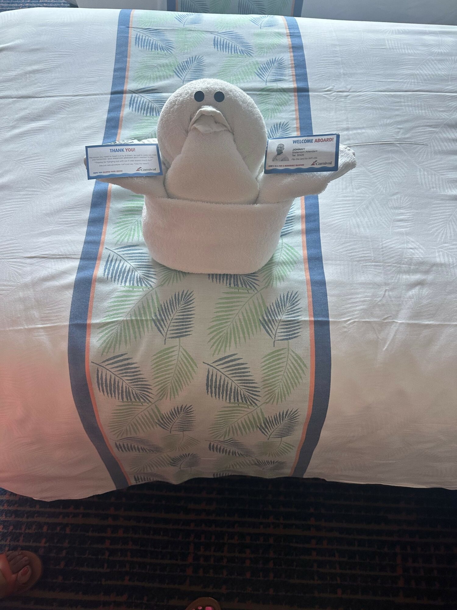 A white ceramic teapot with a lid on a bed with a leaf-patterned bedsheet, viewed from the side.