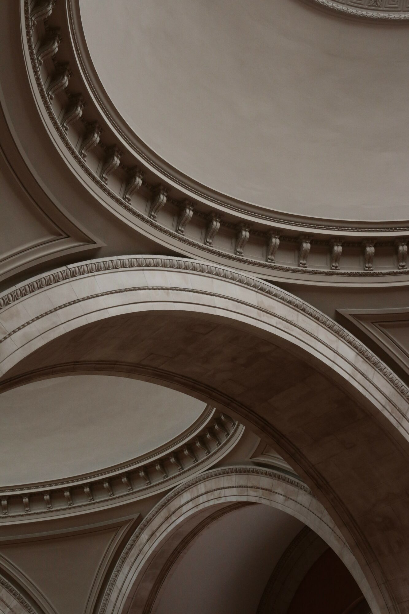 View of ornate architectural arches and domed ceiling with decorative molding, in neutral tones.