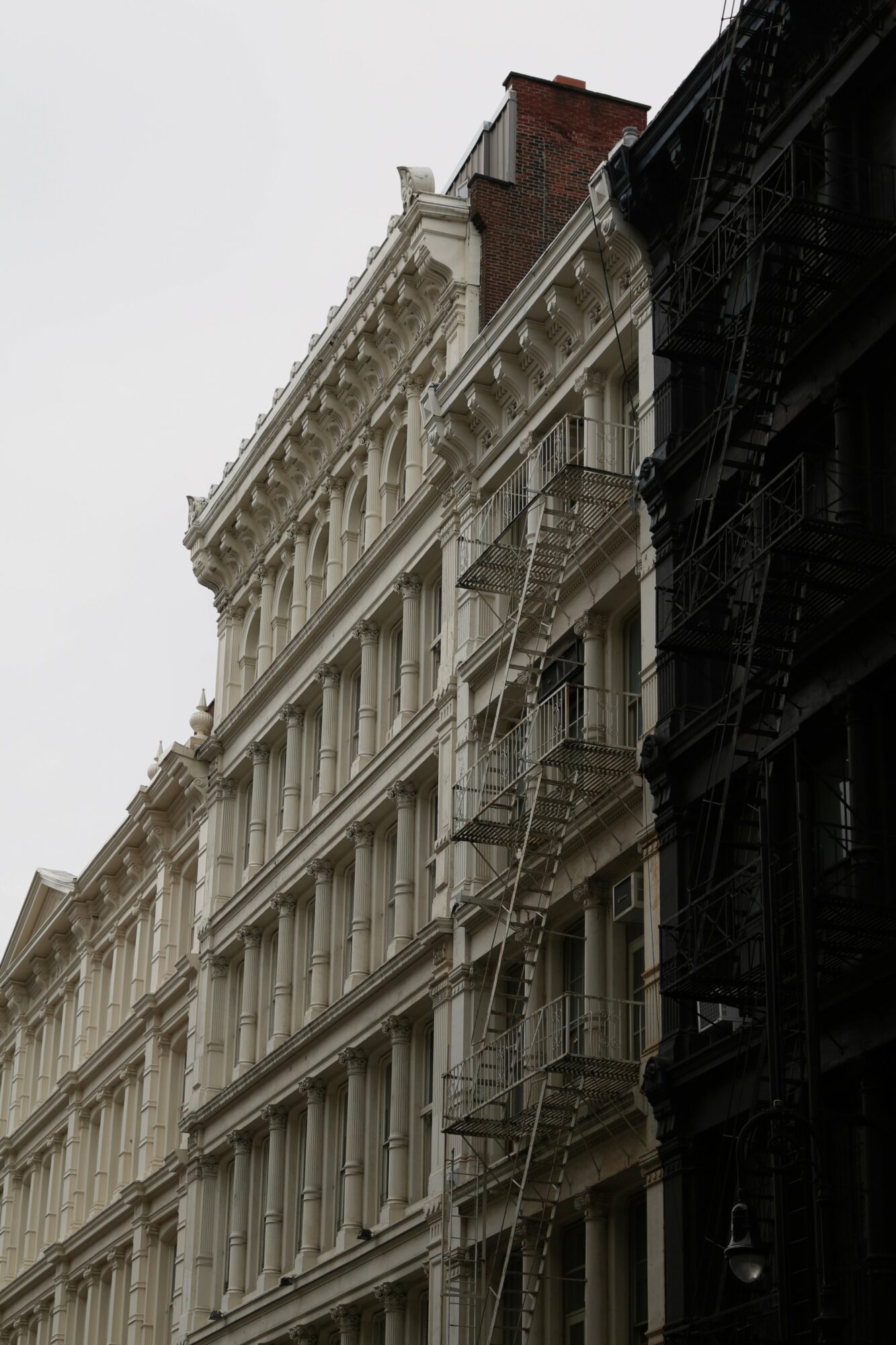 Multiple-story building with ornate architectural details and fire escapes on the facade, viewed from below against a cloudy sky.