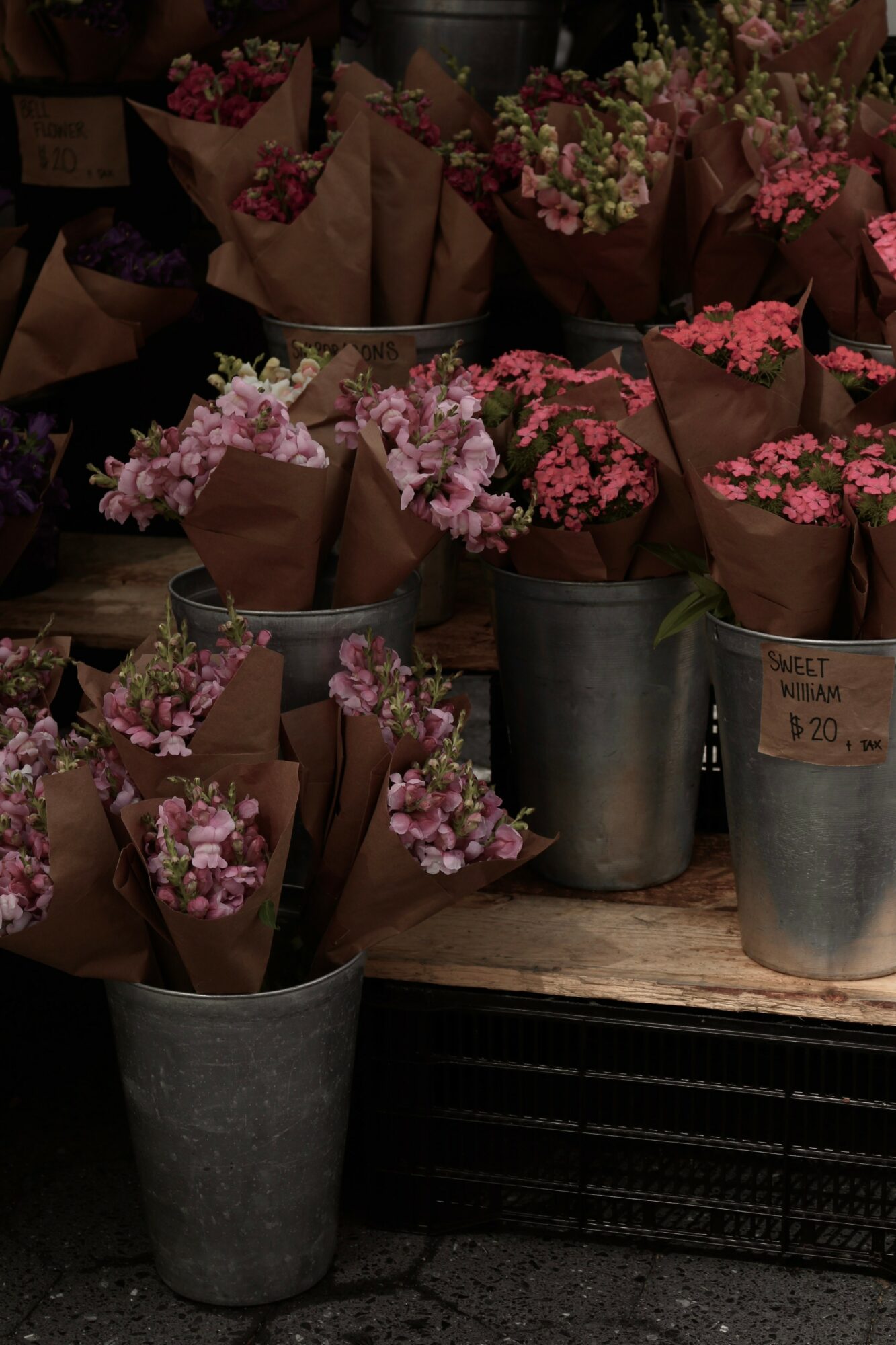 Multiple small flower bouquets in brown paper wrapping and metal buckets on a wooden surface.
