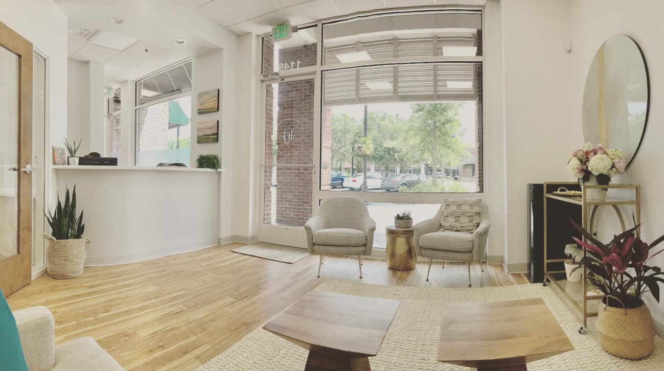 Living room with large window, two armchairs, a small table, and a black console with flowers, hardwood floor, and a mirror.