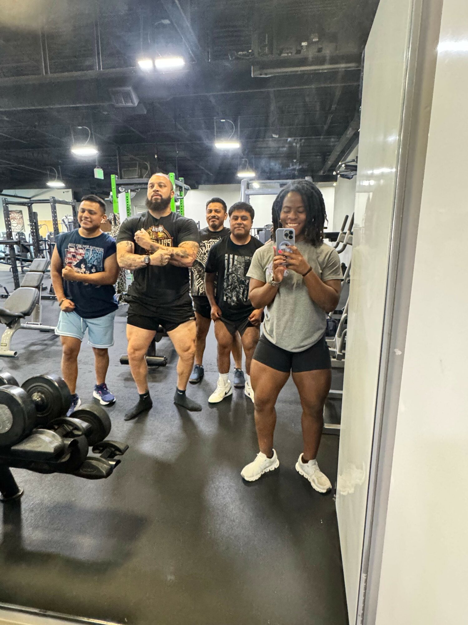 Group of five women taking a mirror selfie in a gym, with exercise equipment visible in the background.