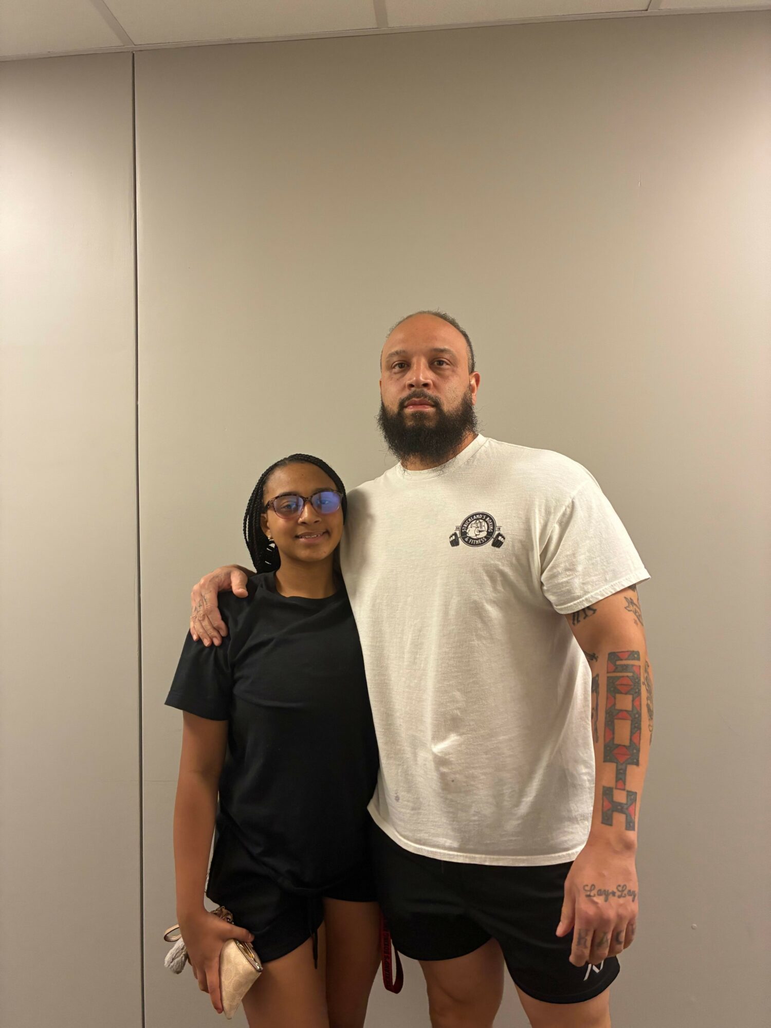 A man with a beard and tattoos on his arm stands next to a woman with glasses and long dark hair, both smiling.
