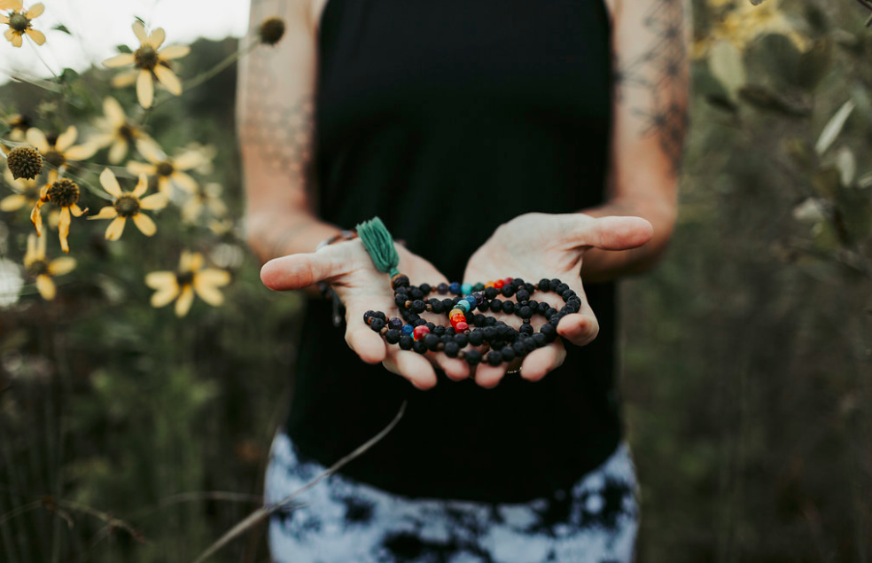 Person holding a handful of berries outdoors with flowers in the background, wearing a black top and patterned pants.