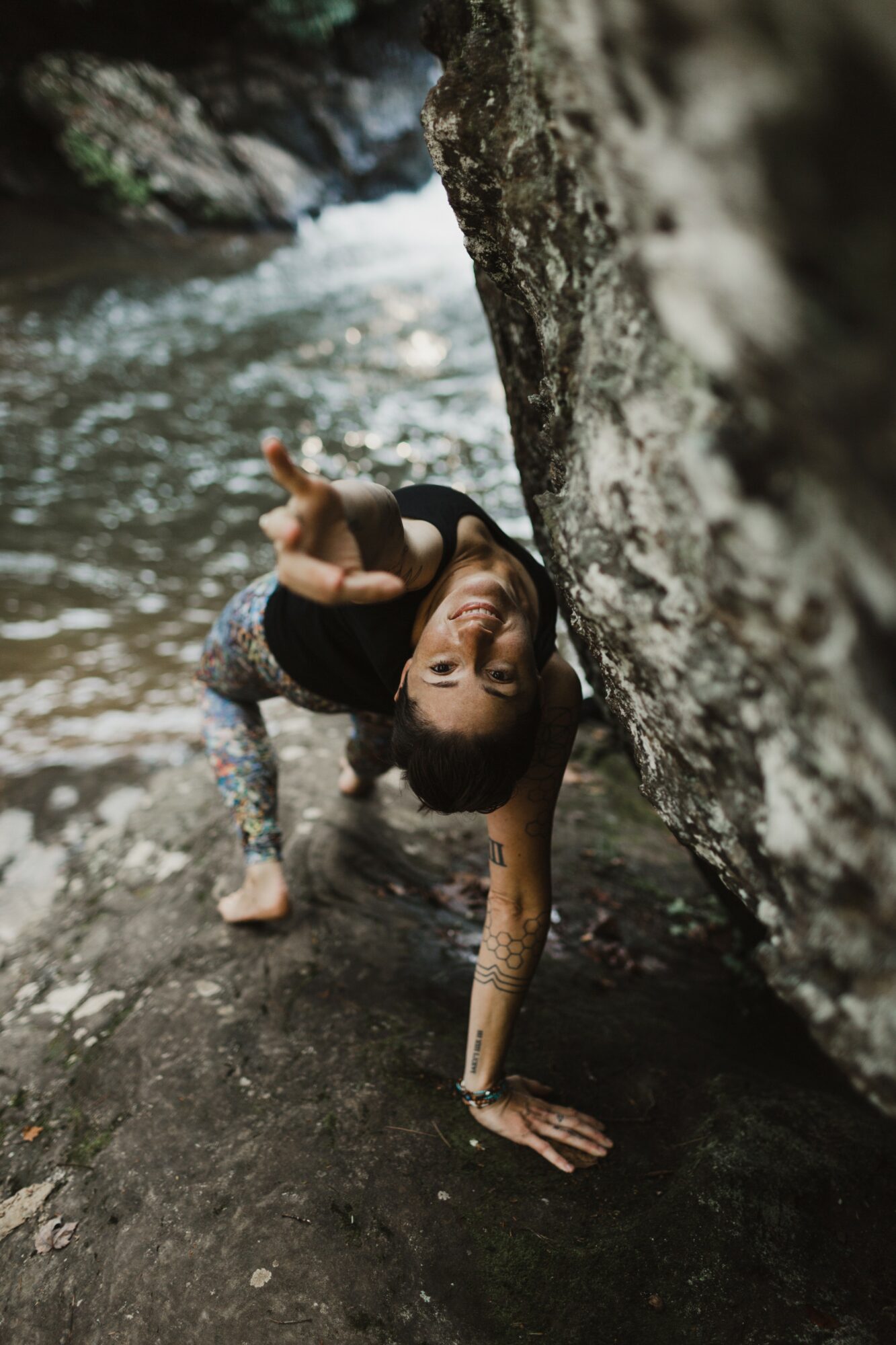 Person performing a handstand on a rock near a river, with a large rock wall behind them.