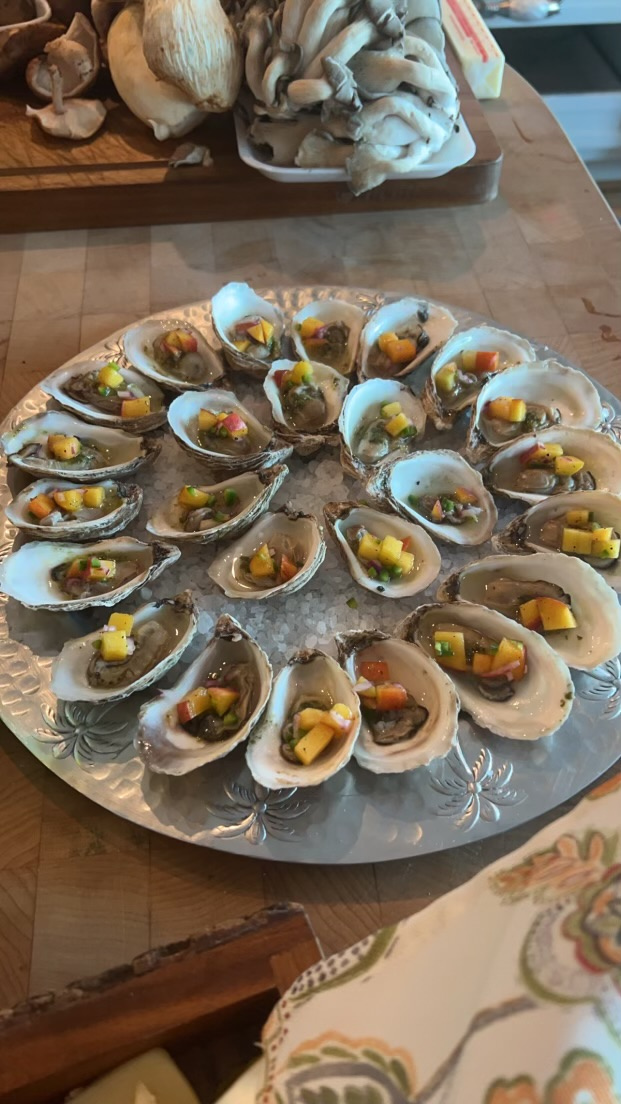 A large silver tray holds multiple small seafood appetizers topped with yellow garnish, on a wooden table.