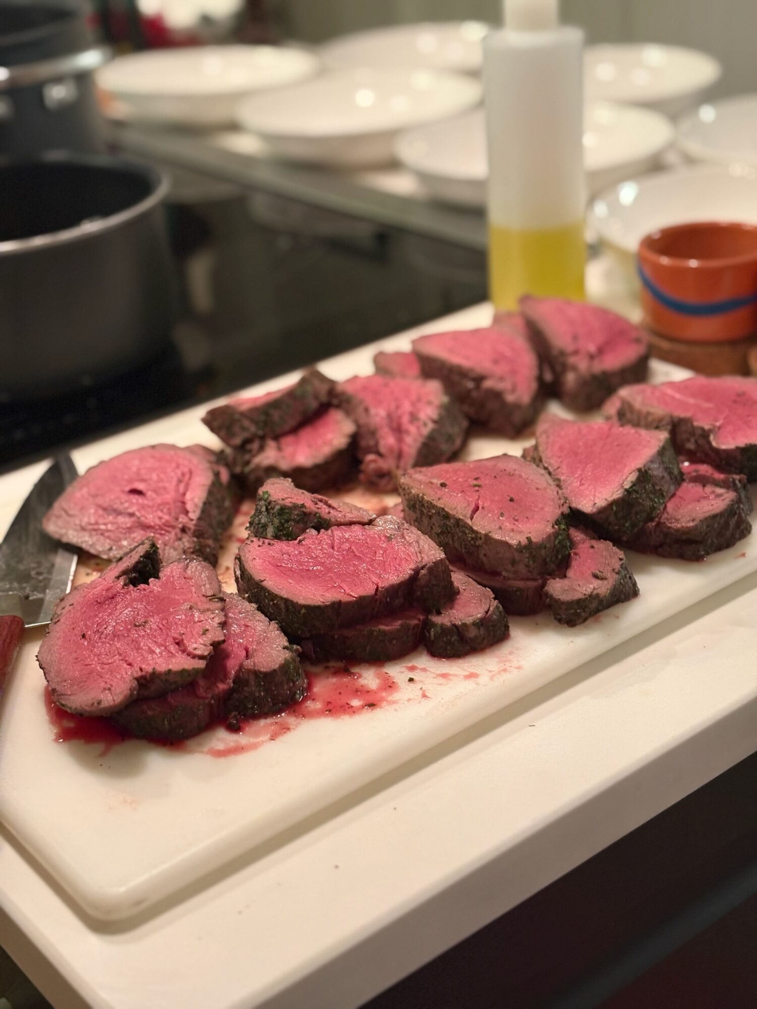Sliced beef Wellington with pink interior and dark crust on a white platter in a kitchen setting.