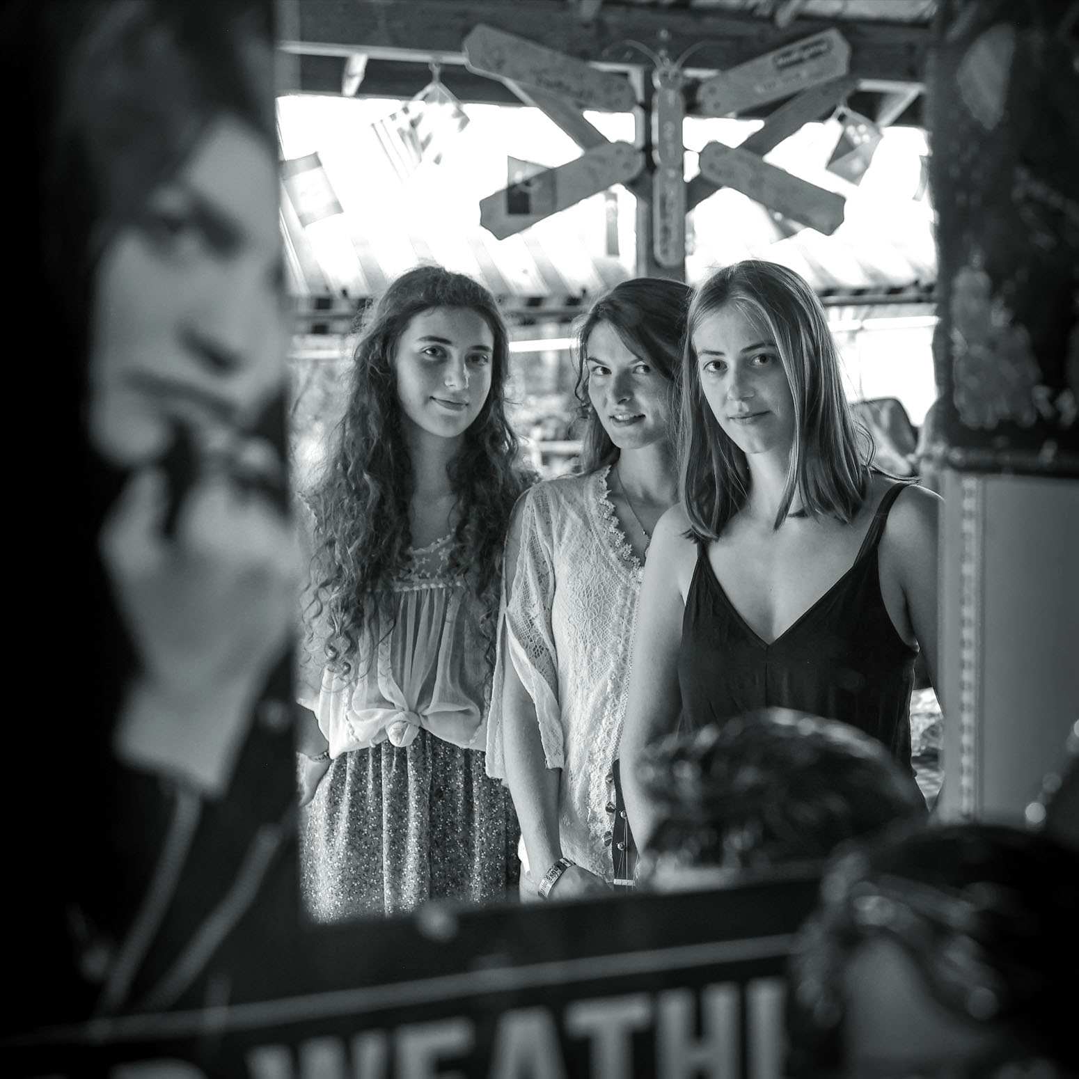 Three women standing together, looking at a person in the foreground, with amusement park rides in the background.