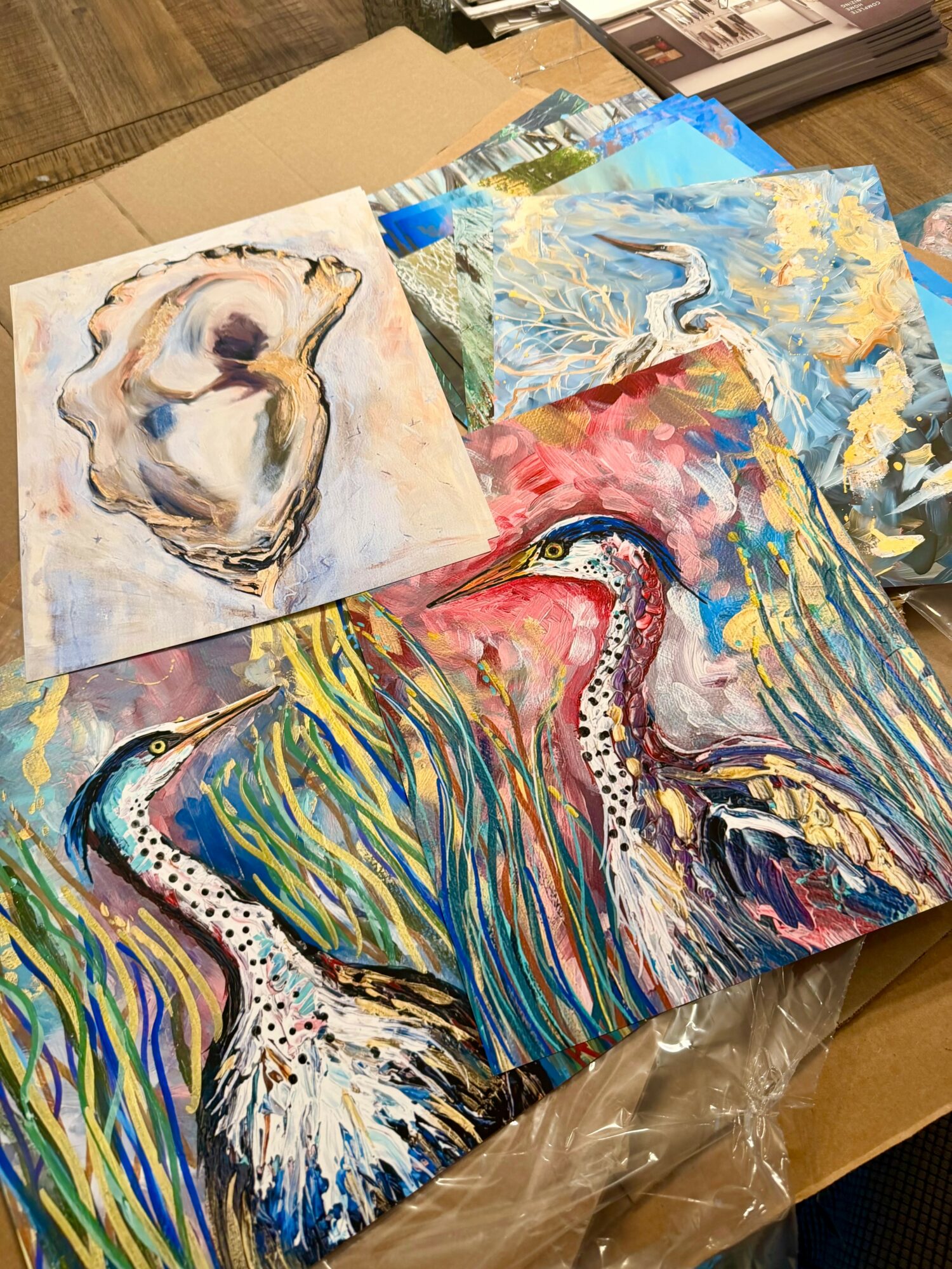 Two colorful paintings of swans with vibrant, abstract backgrounds, placed on a table with art supplies nearby.