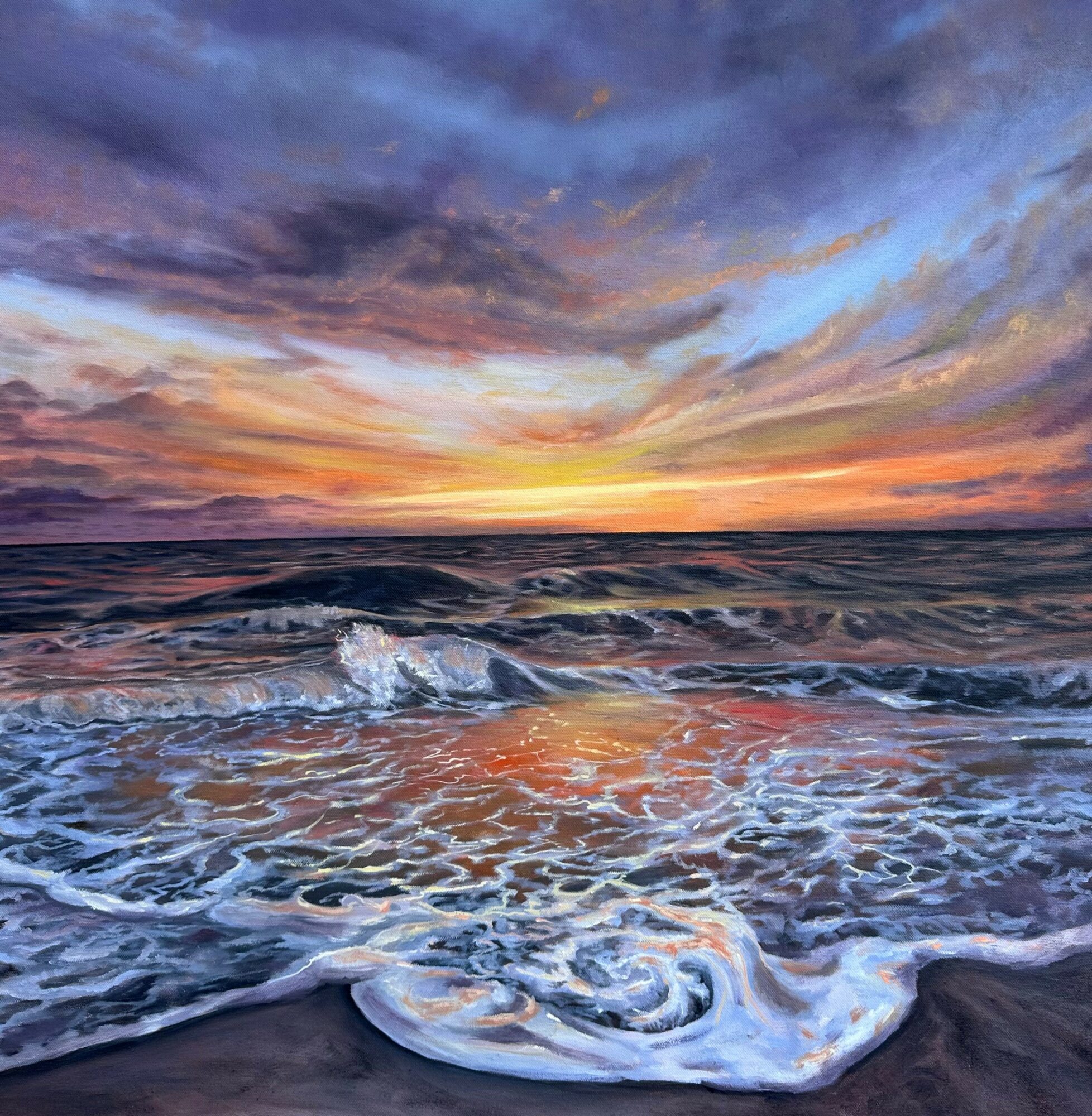 Sunset over ocean with colorful sky and waves crashing on the shore.