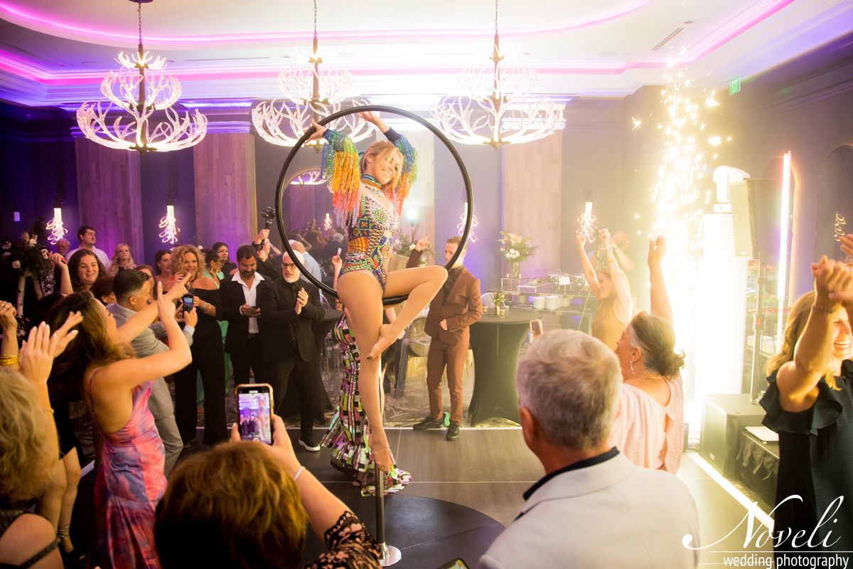 Circus performer on a hoop in front of an audience at a celebration with colorful lighting and sparklers, people cheering.