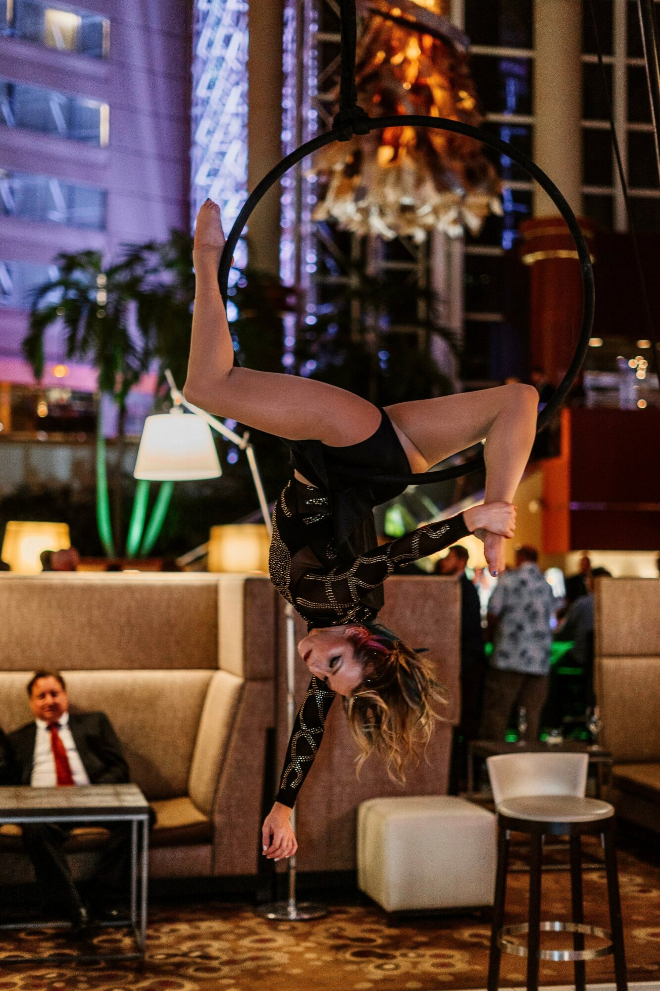 A woman performs a handstand on a chair in a hotel lobby with modern decor and people in the background.