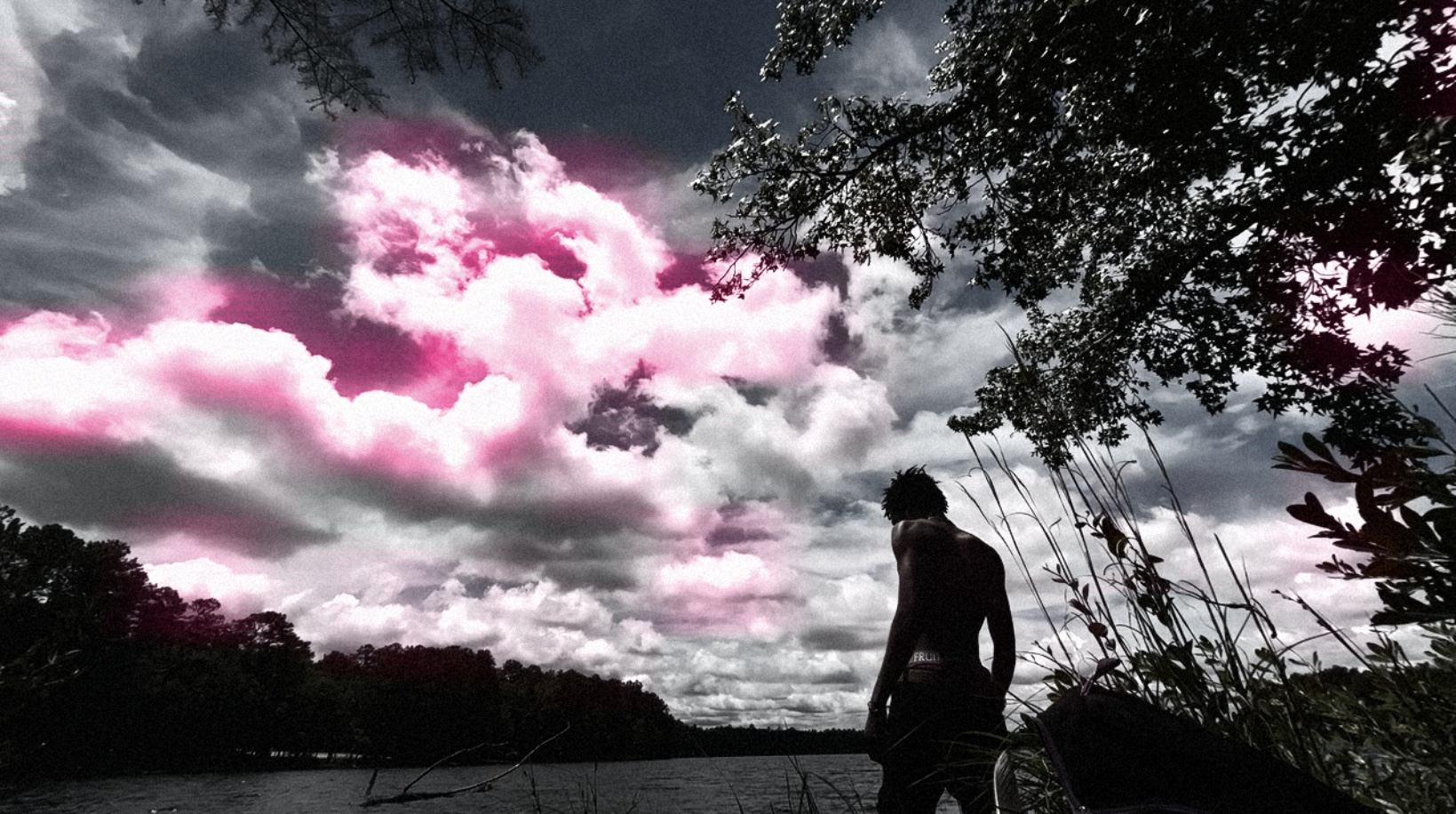 Person standing outdoors with cloudy sky and trees in background, some clouds have pink tint.