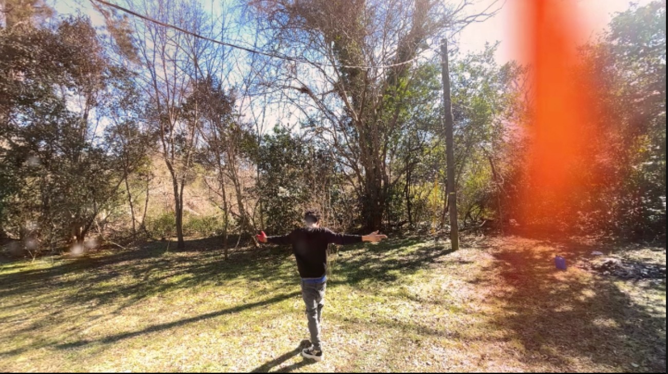 Person standing outdoors with arms outstretched, trees and sunlight in the background.