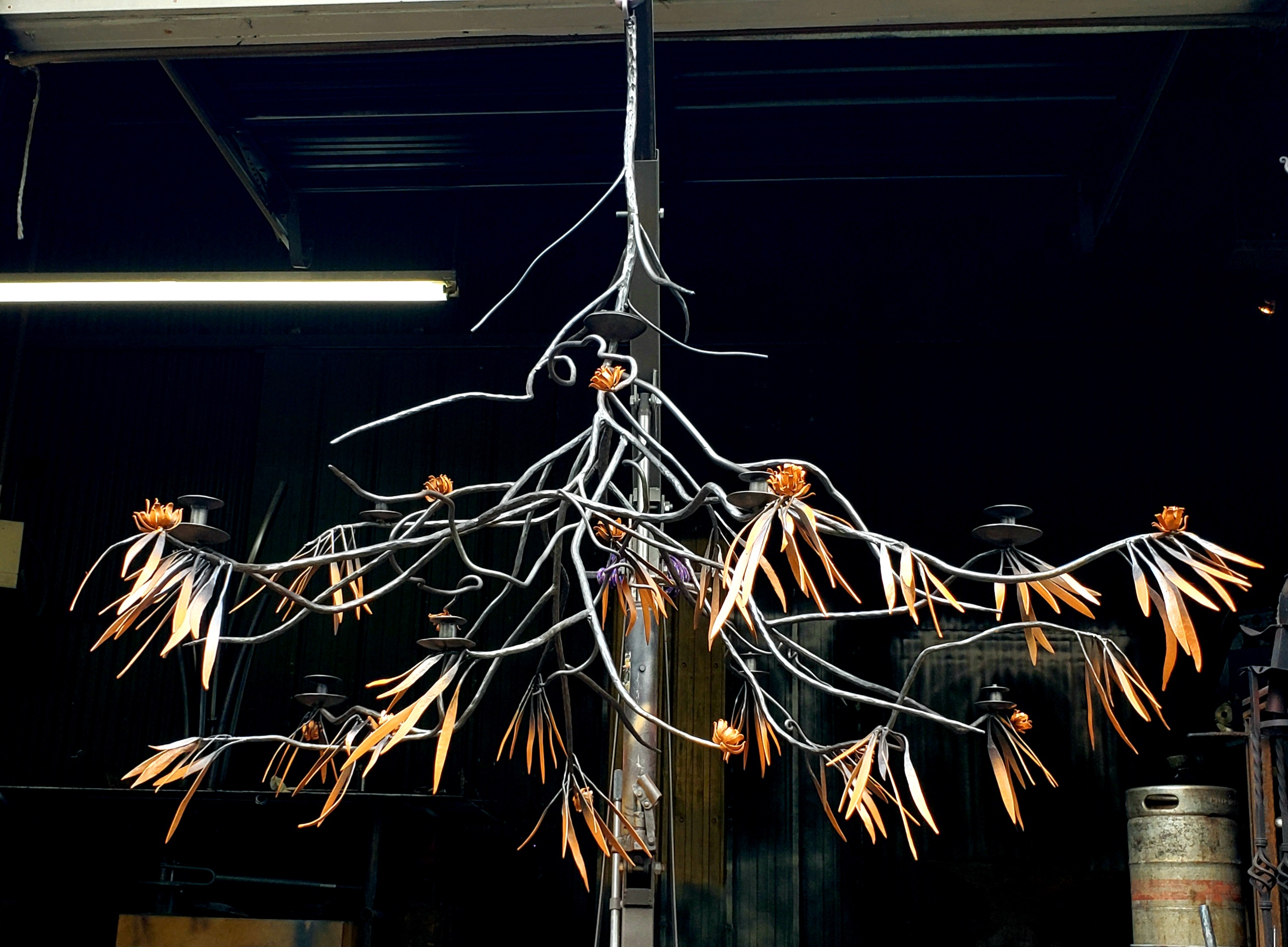 Chandelier made of white branches with orange tips hangs from ceiling in dark room.