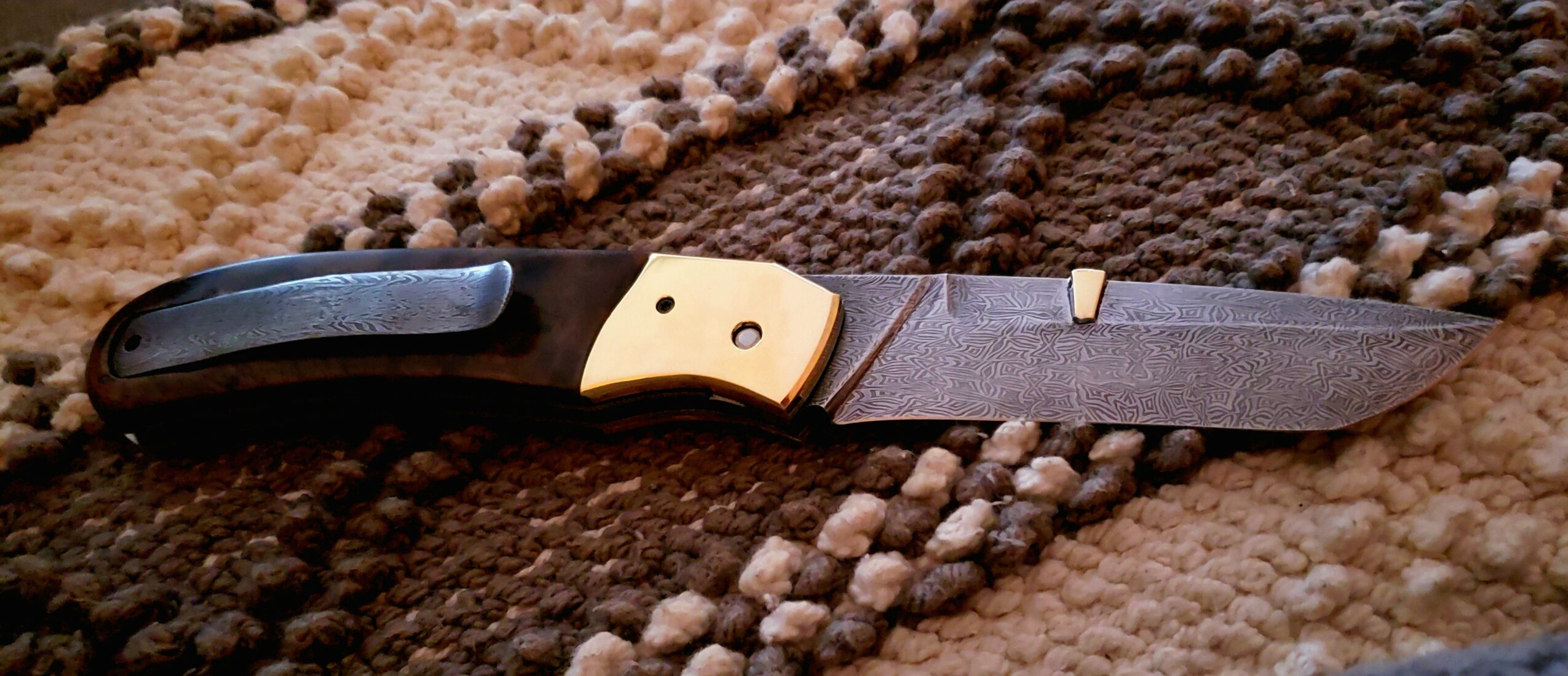Knife with black handle and beige bolster resting on a textured brown and beige fabric