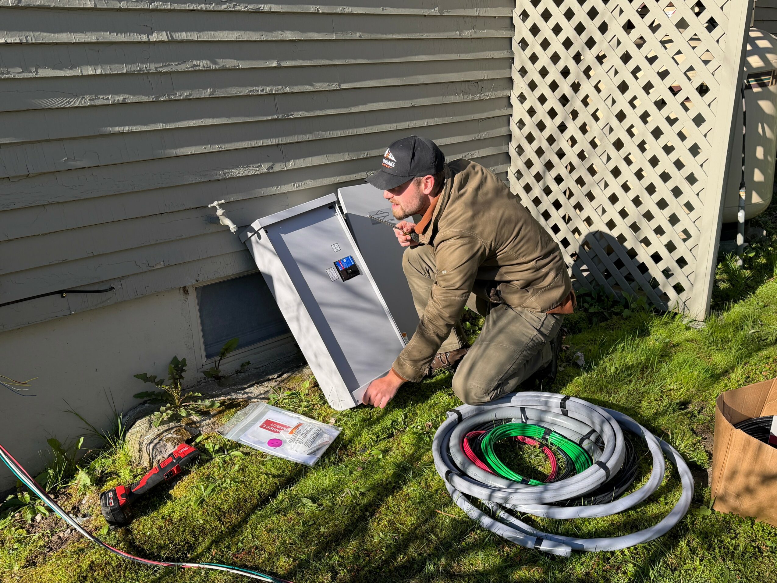 Person installing a solar panel on the ground outside near a house, with gardening tools and coiled hoses nearby.
