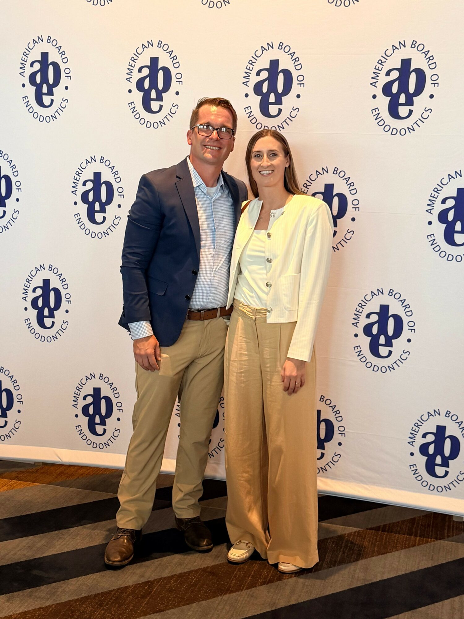 Two people standing in front of a backdrop with the Board of Education logo, smiling and posing for the photo.