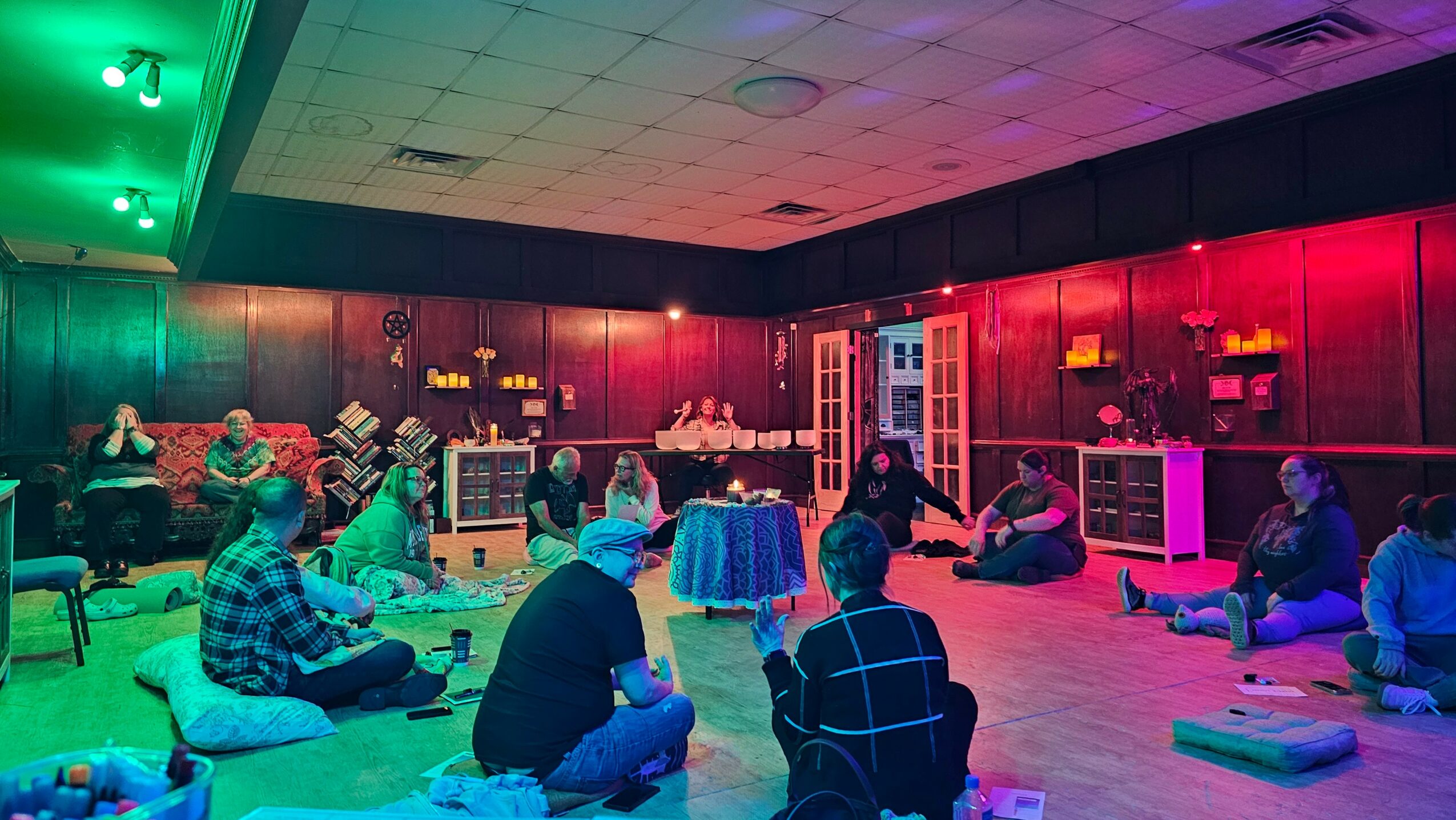 People sitting on cushions in a dimly lit room with colorful lighting, some with laptops or books, engaging in a group activity.