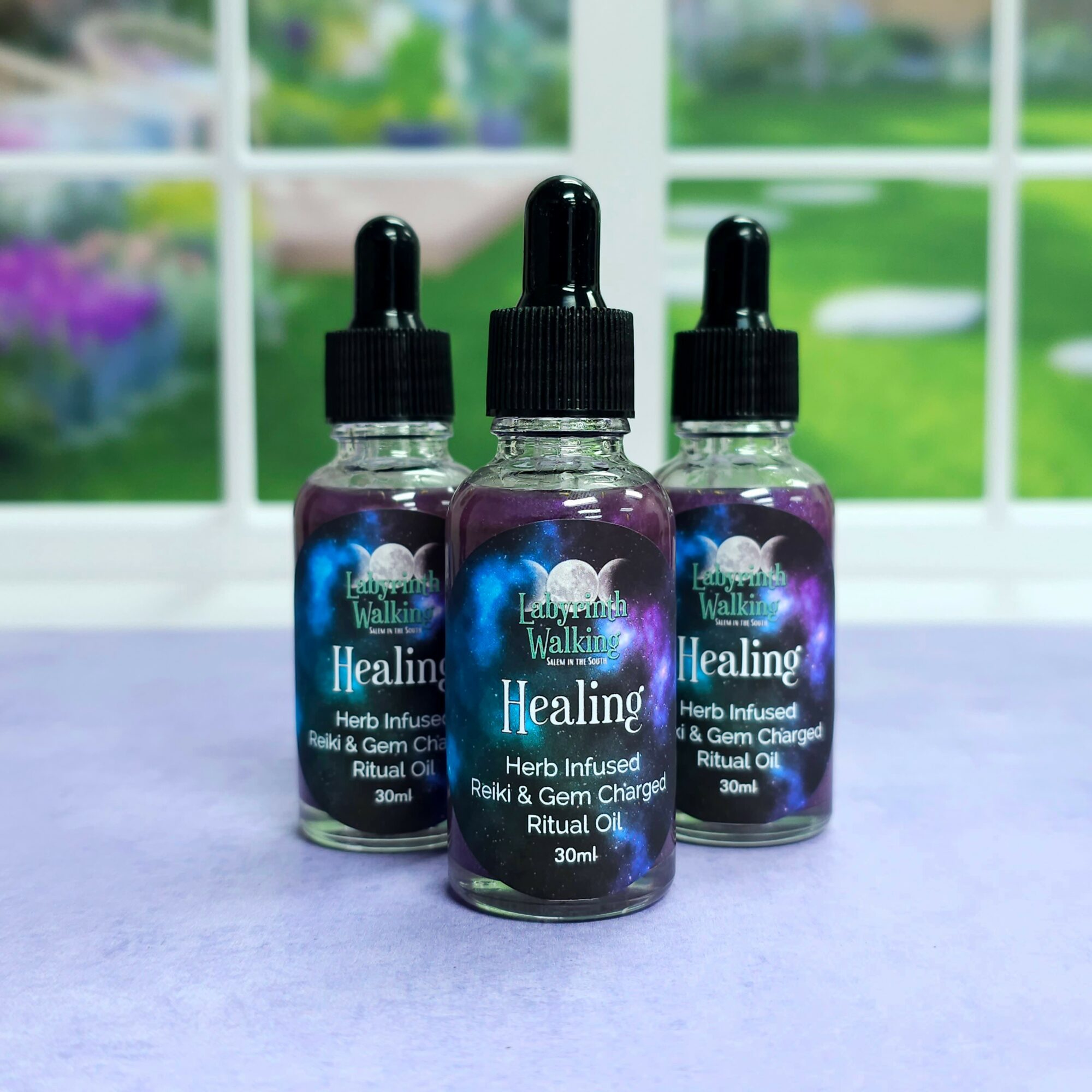 Three small bottles of herbal infused healing oil with dropper caps, placed on a purple surface with a window and garden background, 20 words