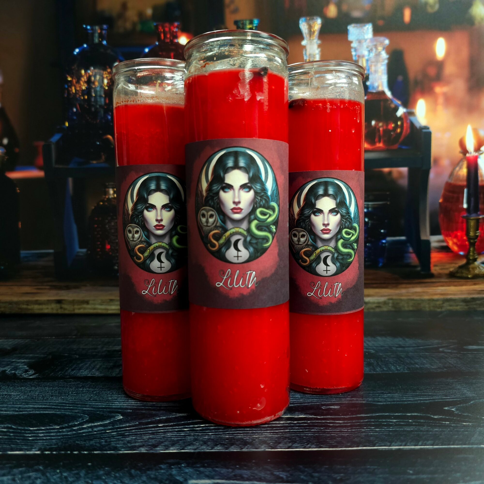 Three red candles with labels featuring a woman's face and green snakes, on a dark wooden surface, with a blurred background.