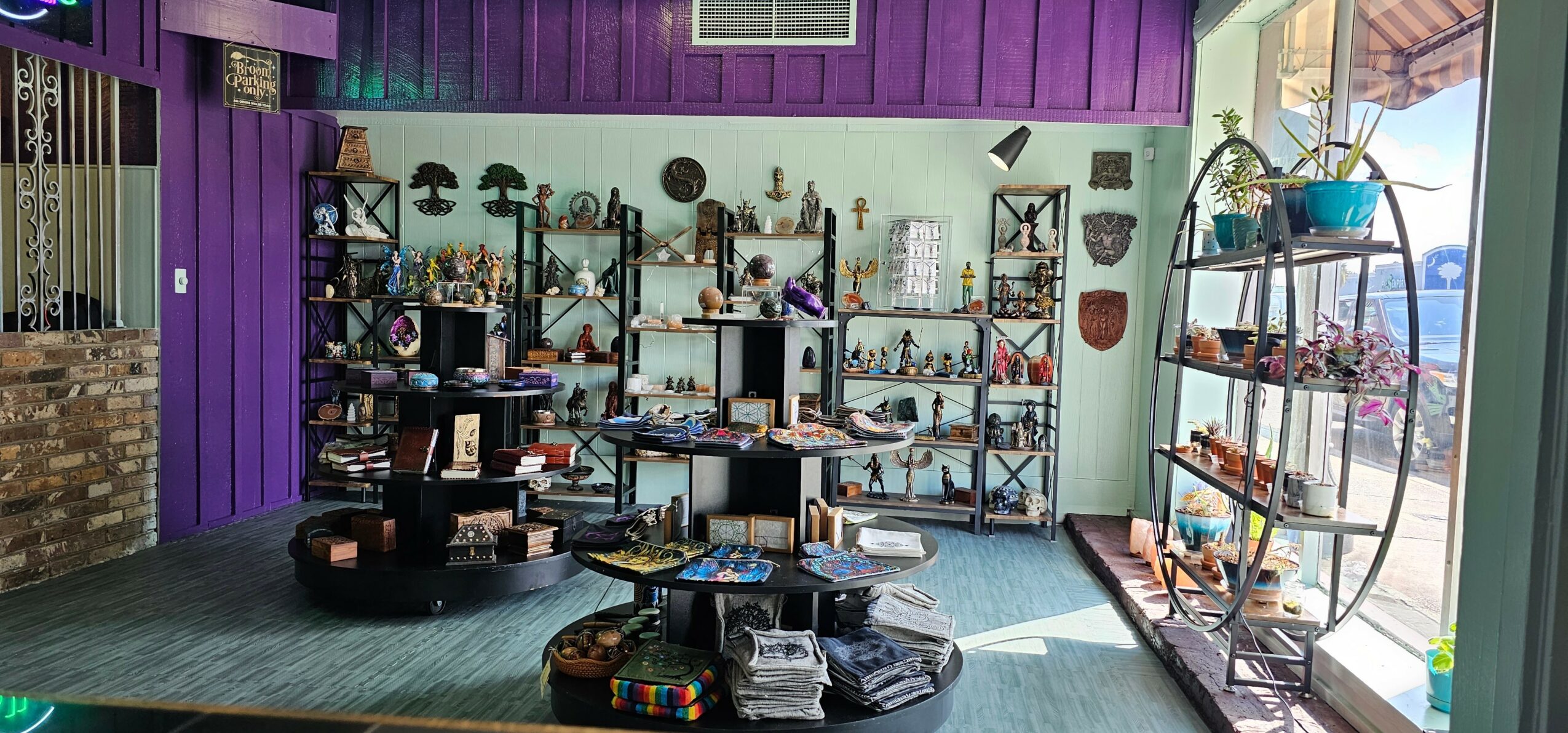 Interior of a store with shelves displaying various items, purple and green walls, and a large window letting in natural light.