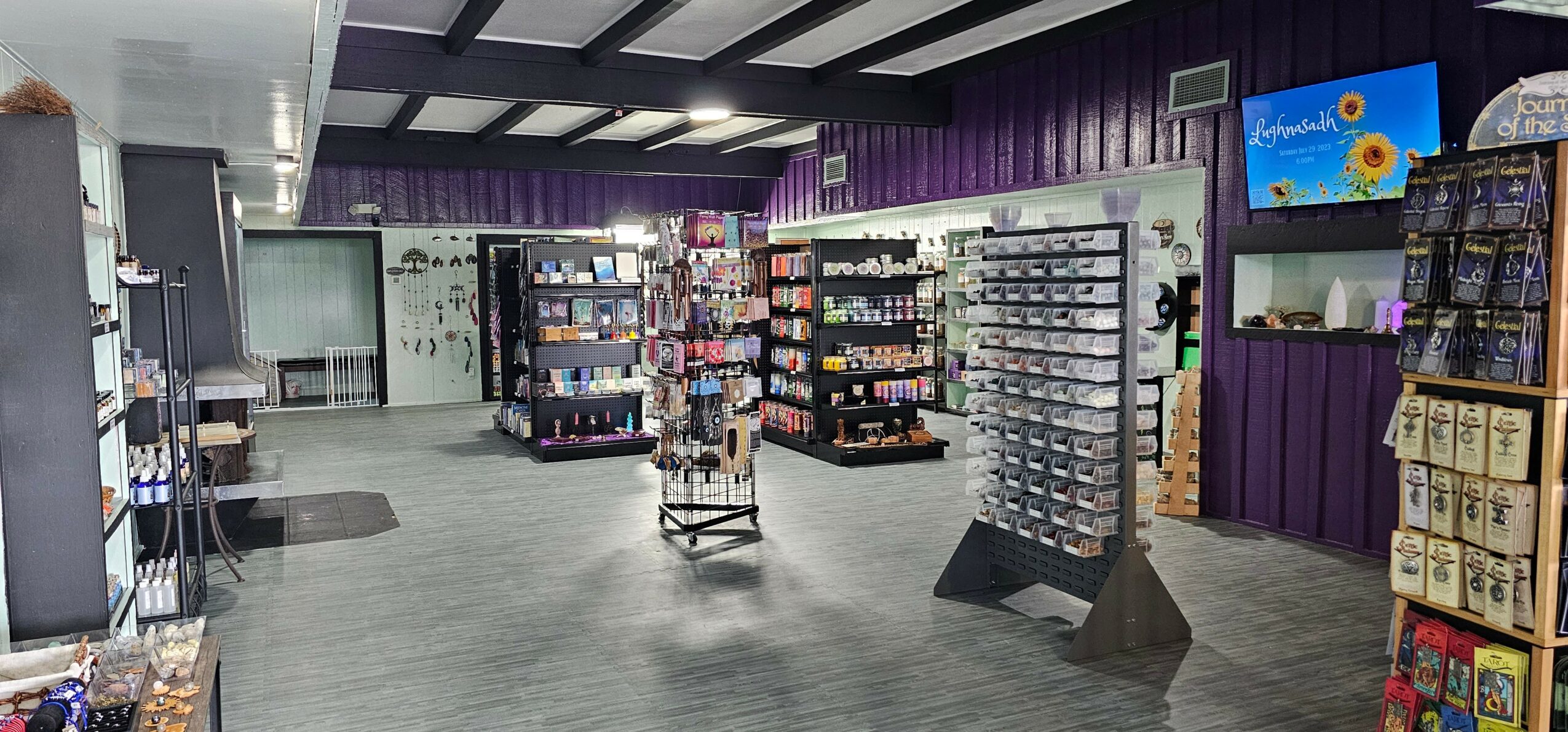 Interior of a store with shelves stocked with various products, purple walls, and a television screen on the wall.