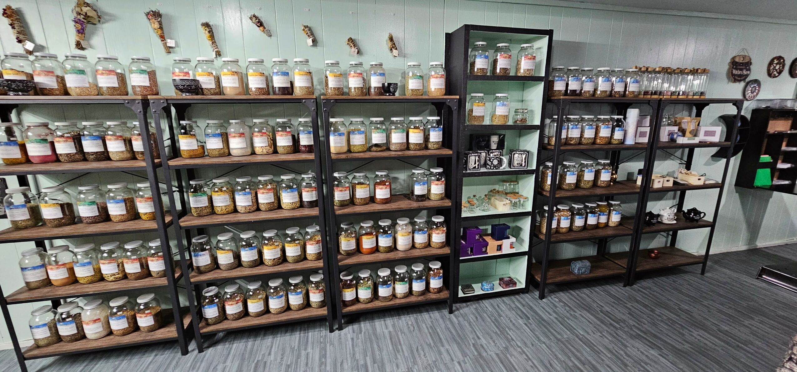 Shelves filled with jars and containers in a store, with a gray carpeted floor and a wall with hanging items.