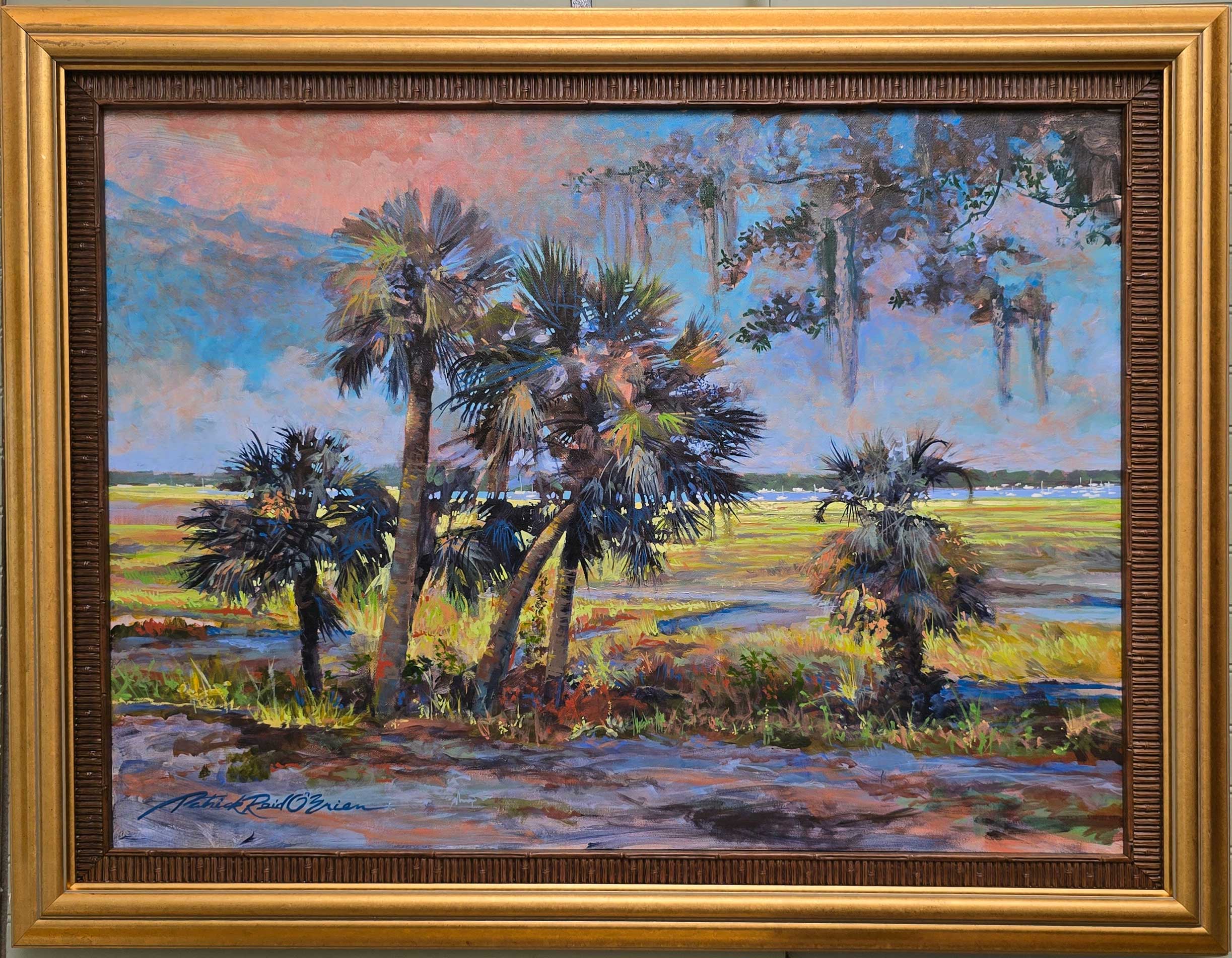 Landscape painting of palm trees near water with a colorful sky, framed in a gold frame.
