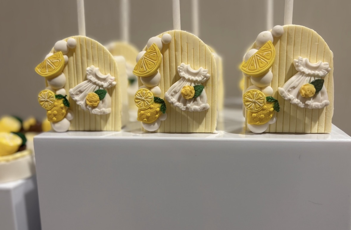 Three lemon-themed desserts with lemon slices, whipped cream, and yellow decorations on a white surface.