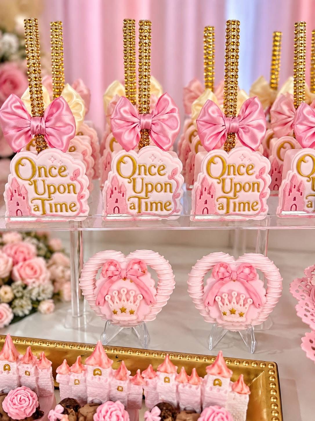 Decorative pink and gold themed party treats with bows, 'Once Upon a Time' signs, and pink princess crowns, arranged on a display.