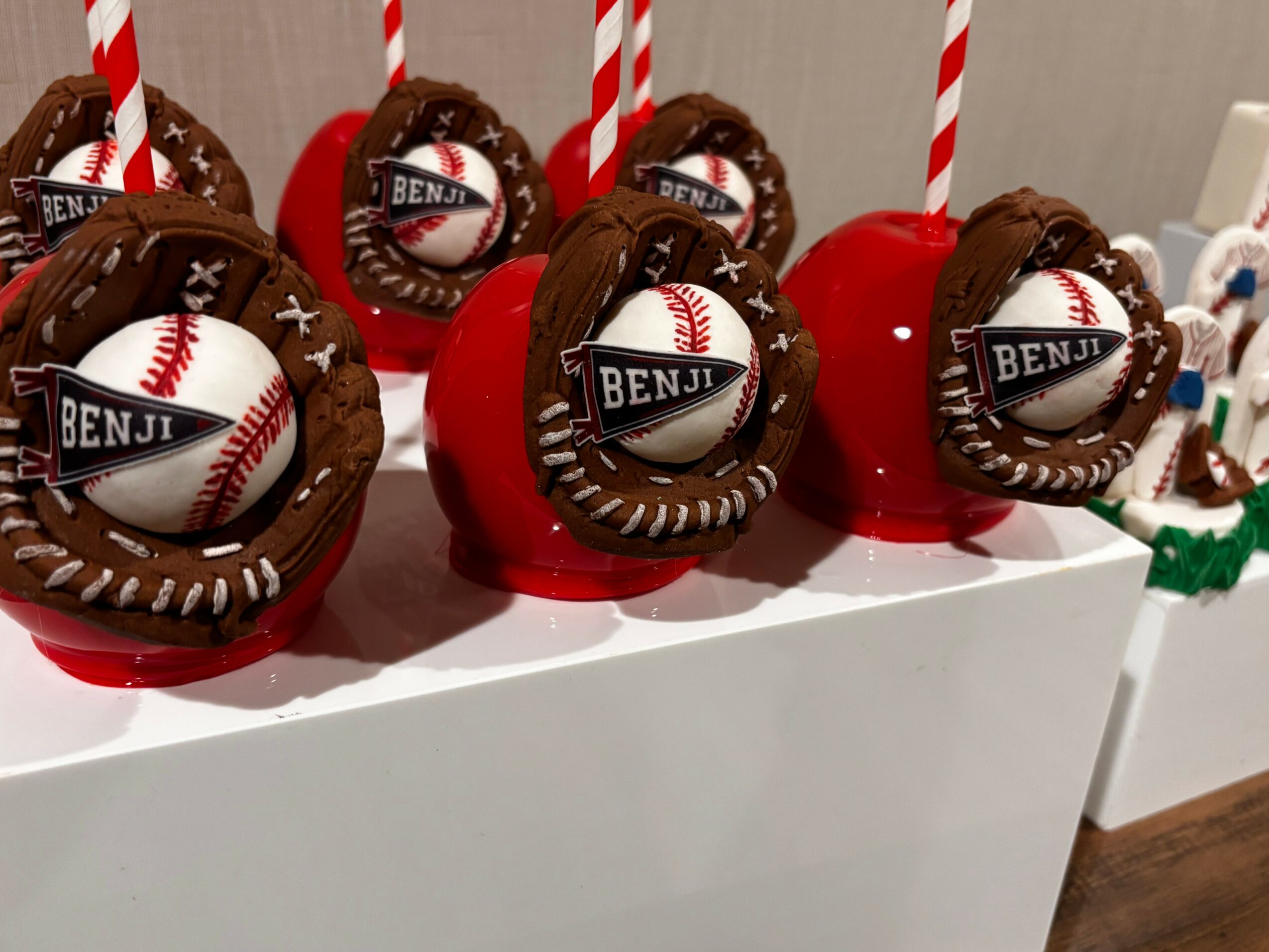 Chocolate desserts with baseball-themed decorations, red apples, and striped straws on a white surface.