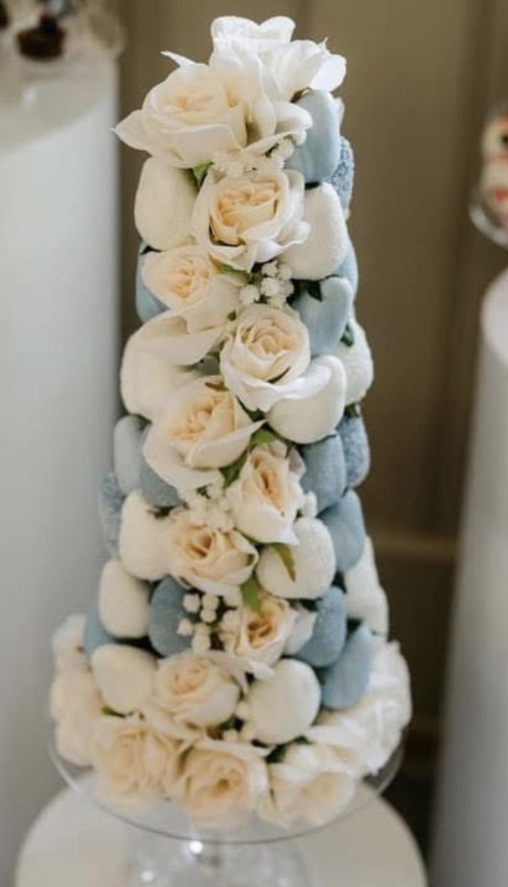 Tall floral arrangement with white roses, blue and white decorative elements, and small white flowers on a stand.