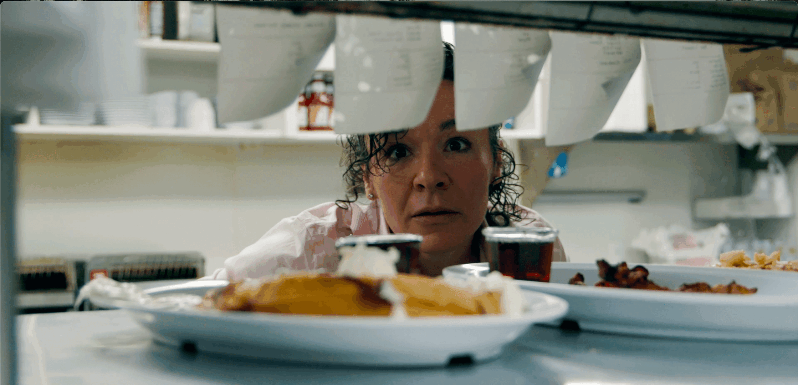 Woman looking at food on a table, viewed from below, with plates of food in foreground.