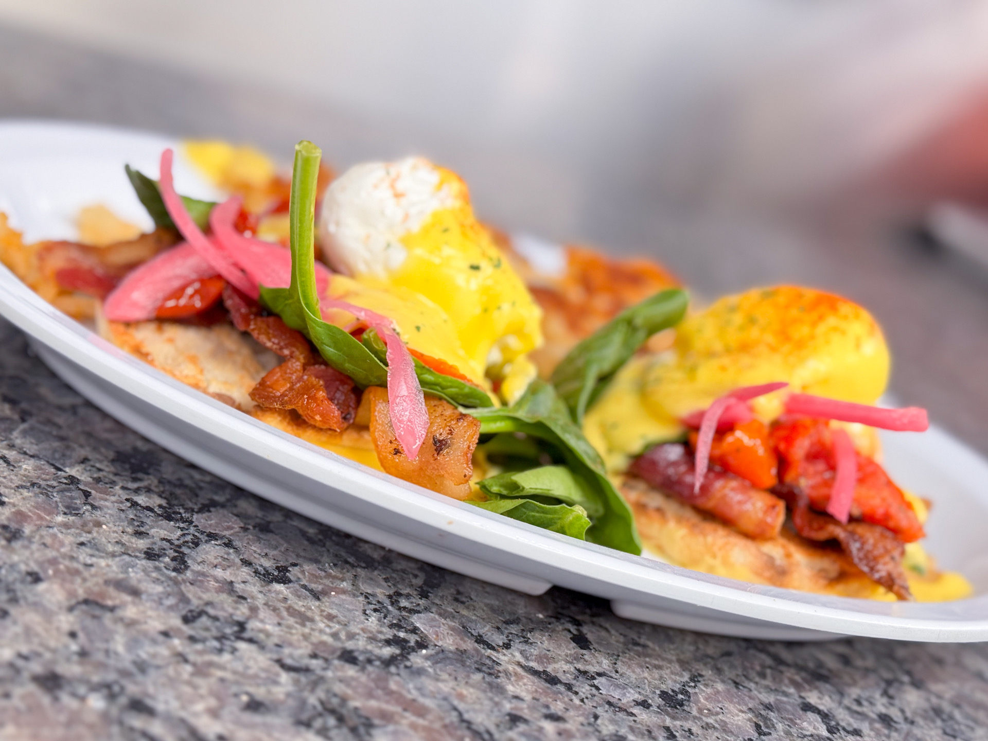 Plate with eggs, bacon, pickled vegetables, and greens on a granite surface.
