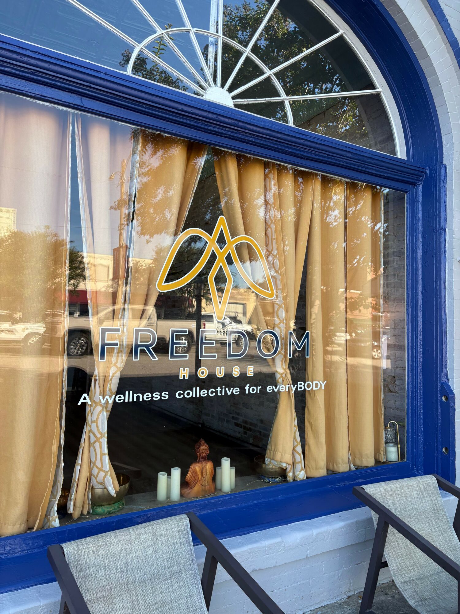 Curtains with the word 'FREEDOM' and a logo, outside a window with a blue frame, reflecting trees and buildings.