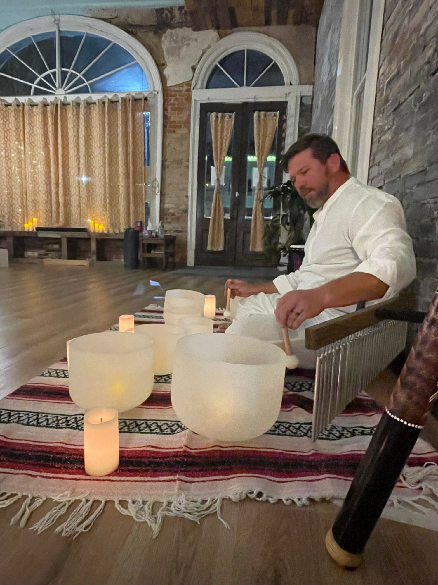 Person sitting at a table with candles and decorative objects, in a room with stone walls and a window with curtains.