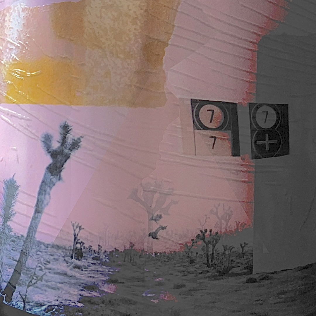Desert landscape with trees, mountains, and a pink sky, featuring a sign with the number 7, 20 words.