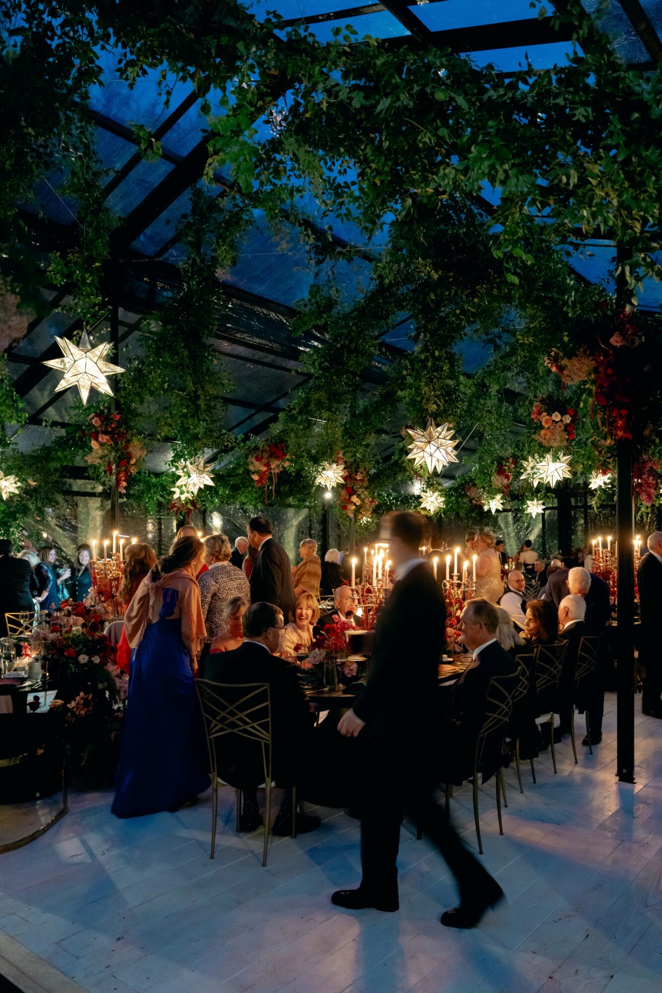 People dining in a decorated indoor space with hanging star-shaped lights and greenery, evening setting, some standing and some seated.